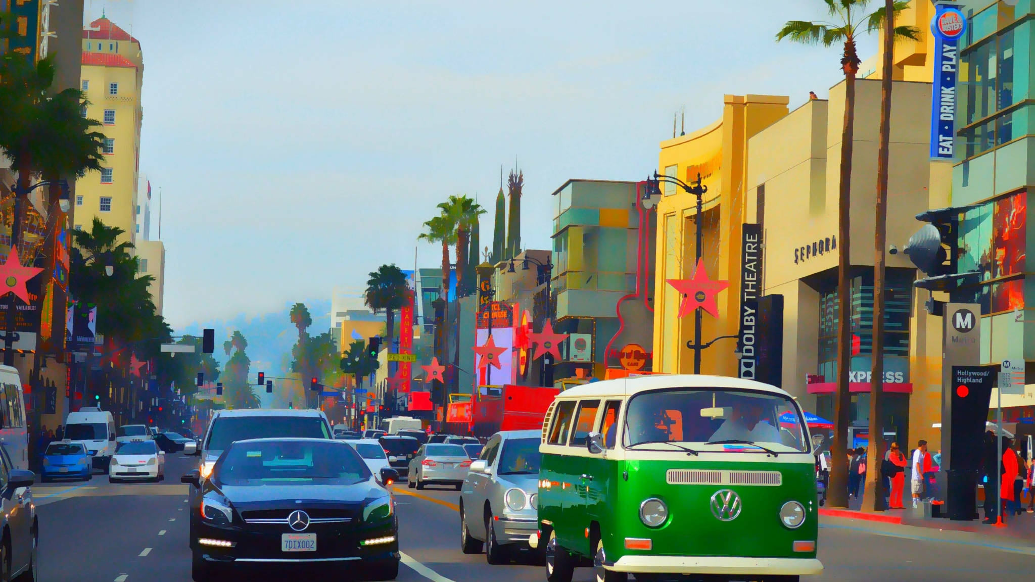 hollywood street 桌布 壁紙 — 一輛充滿活力的綠色復古VW巴士在晴朗的藍天下，行駛在棕櫚樹和標誌性星形標誌林立的繁華好萊塢街道上。