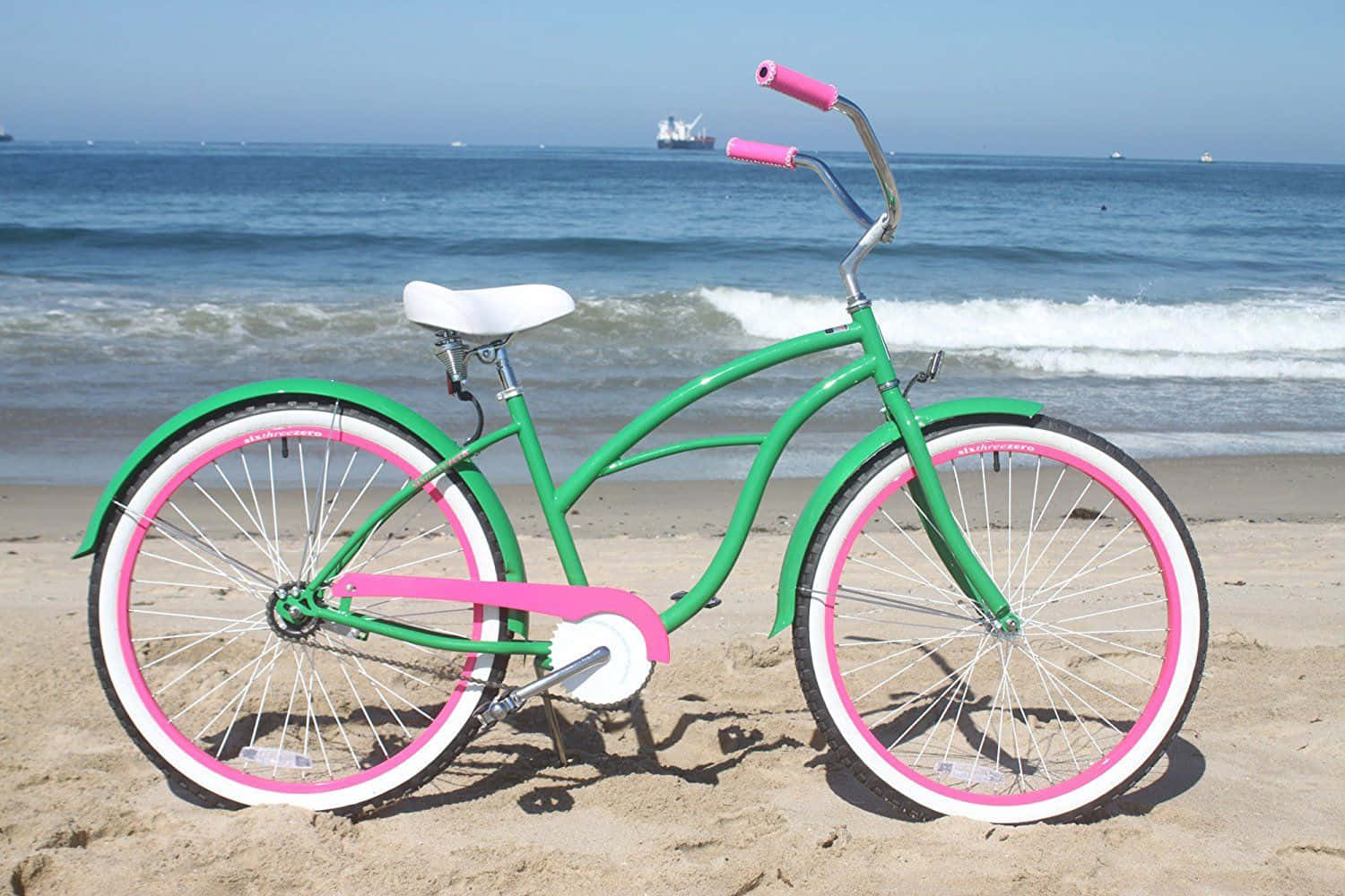 Beach Cruiser 桌布 壁紙 — 一輛充滿活力的綠色沙灘巡洋艦自行車，帶有粉紅色點綴，停靠在沙灘上，旁邊是清澈藍天下拍打的海浪。