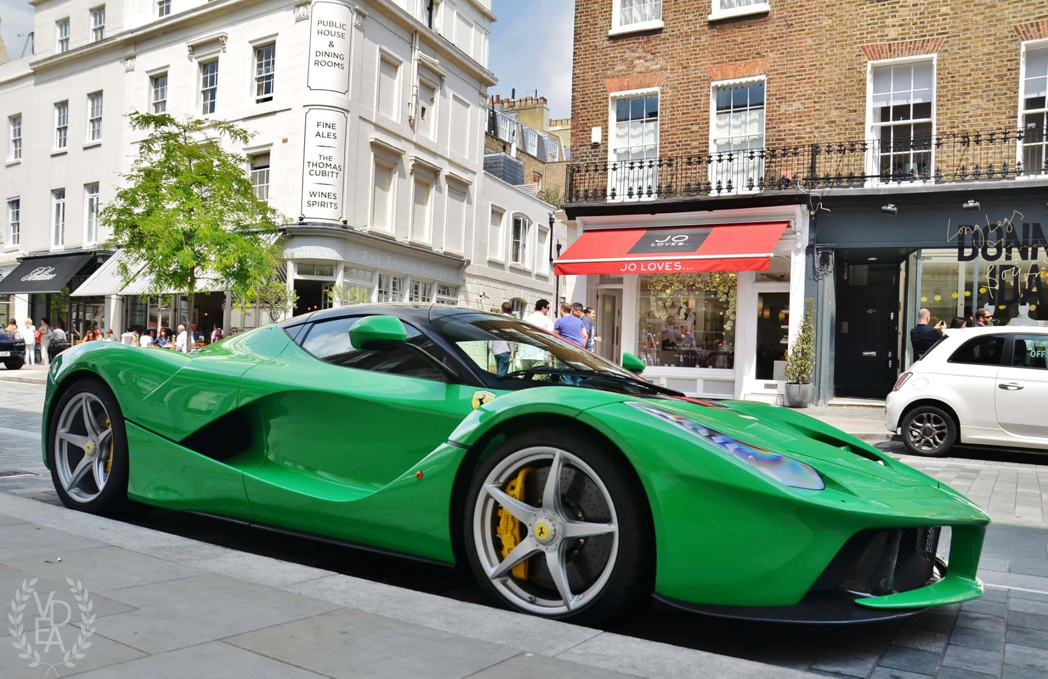 Ferrari Laferrari 桌布 壁紙 — 一輛充滿活力的綠色法拉利LaFerrari停泊在倫敦繁忙的街道上，周圍是歷史悠久的磚砌和白色建築。