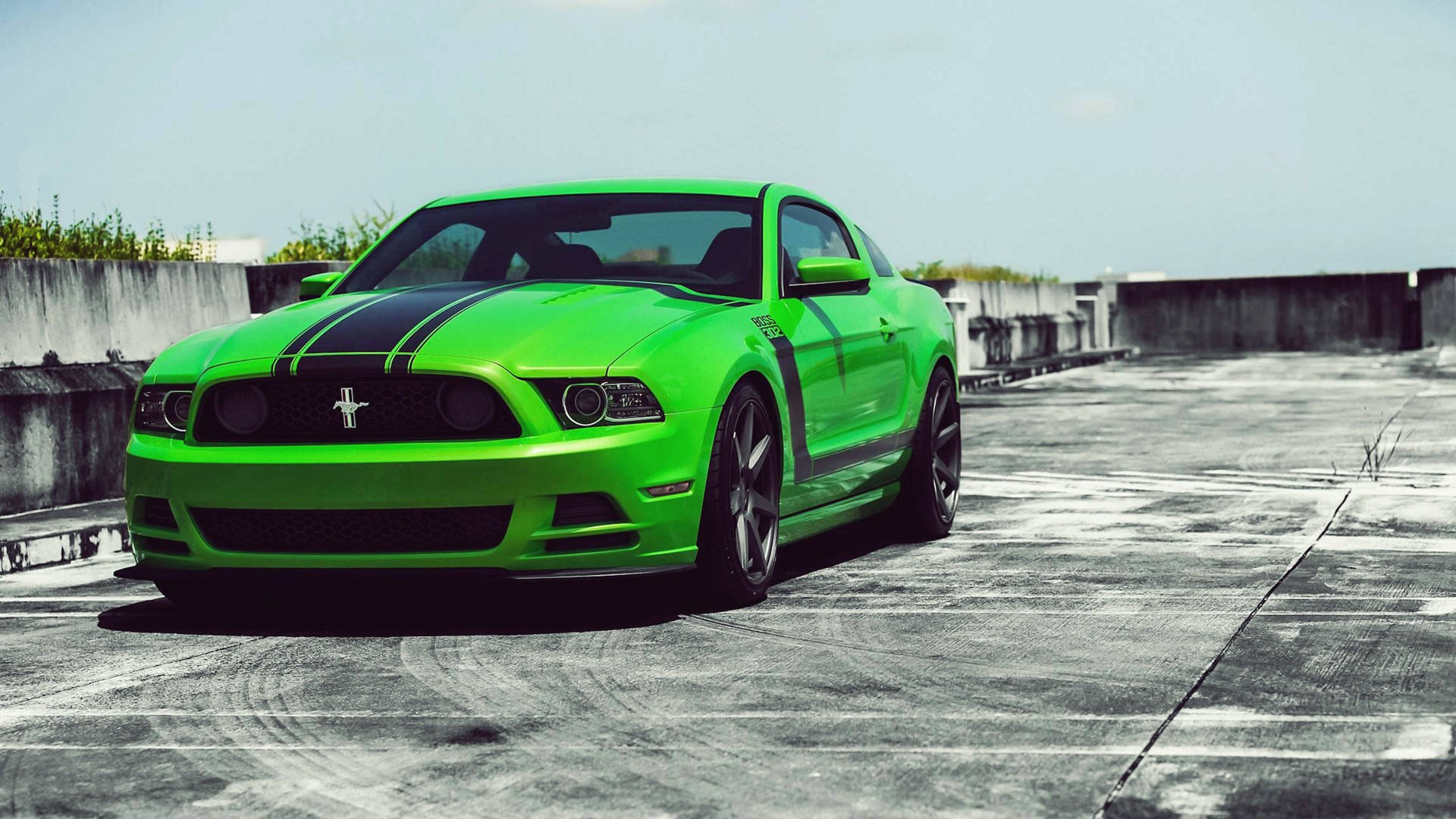 mustang HD 桌布 壁紙 — 一輛充滿活力的綠色福特野馬，帶有黑色賽車條紋，停在風化的混凝土屋頂上，天空晴朗。