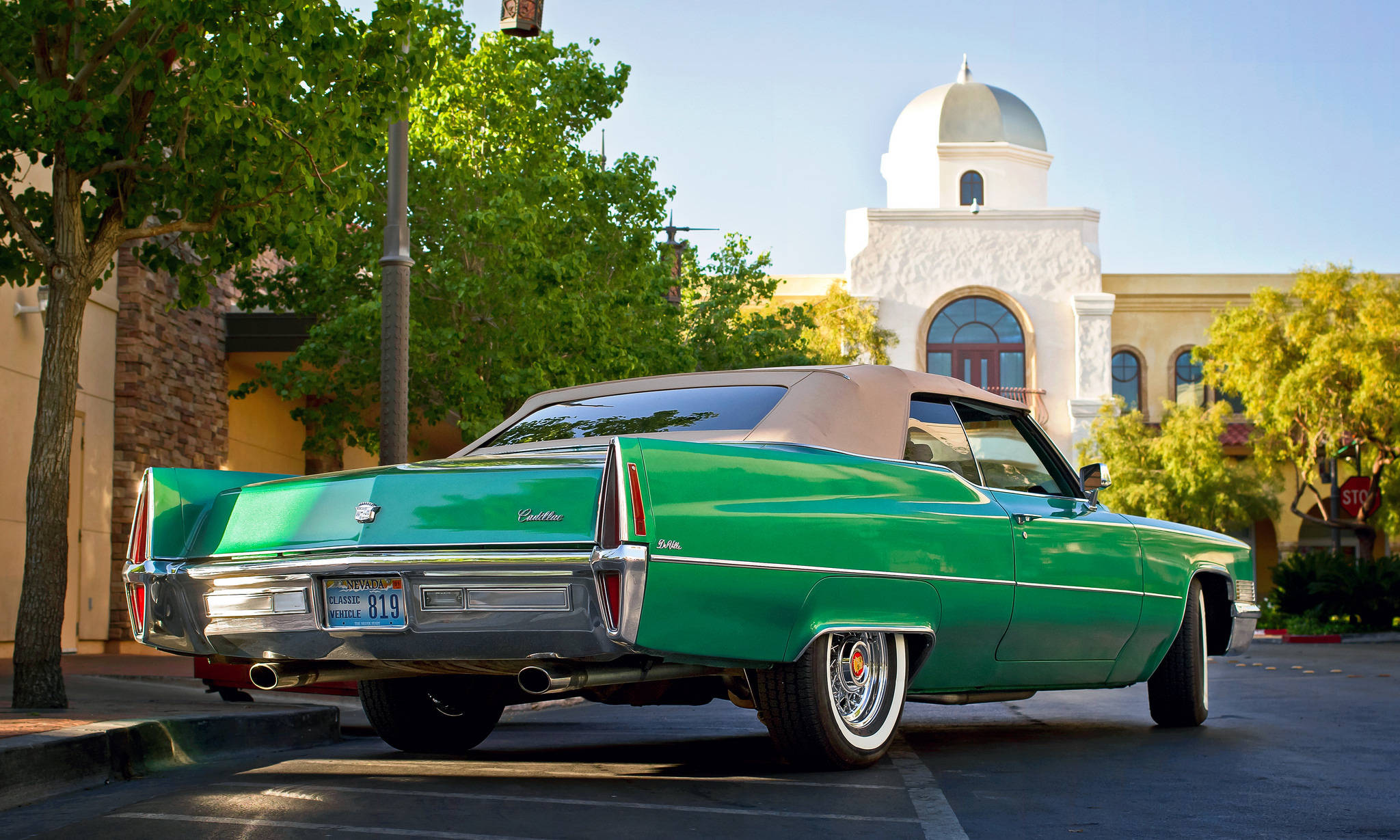 Cadillac 桌布 壁紙 — 一輛充滿活力的綠色經典凱迪拉克敞篷車停放在陽光明媚的城市地段，背景是白色圓頂建築和茂密的樹木。