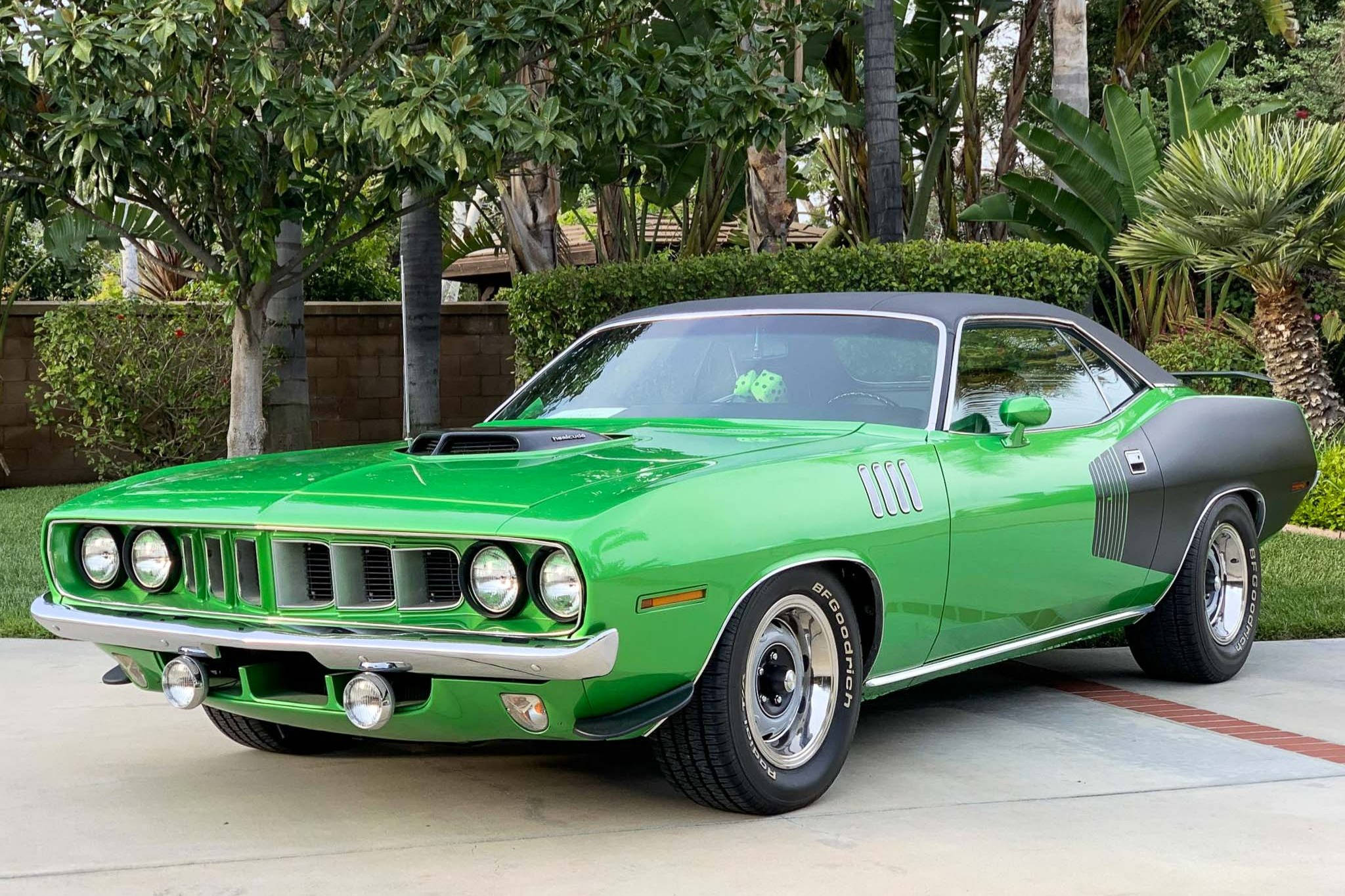 Plymouth Barracuda 桌布 壁紙 — 一輛充滿活力的綠色經典肌肉車，帶有黑色飾邊，停泊在車道上，周圍環繞著茂密的熱帶植物。