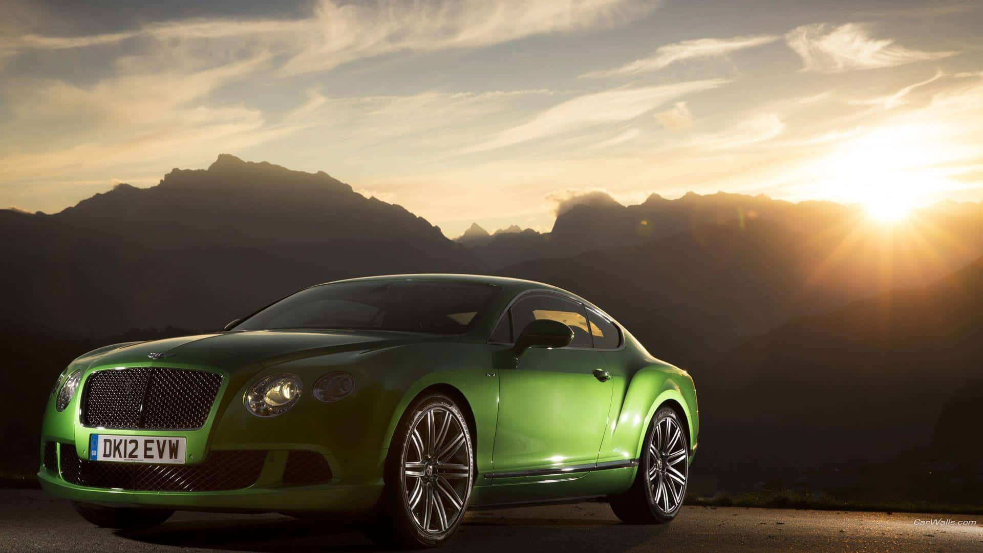 bentley HD 桌布 壁紙 — 一輛充滿活力的綠色賓利 Continental GT 在崎嶇的山景背景下，在金色夕陽下閃閃發光。