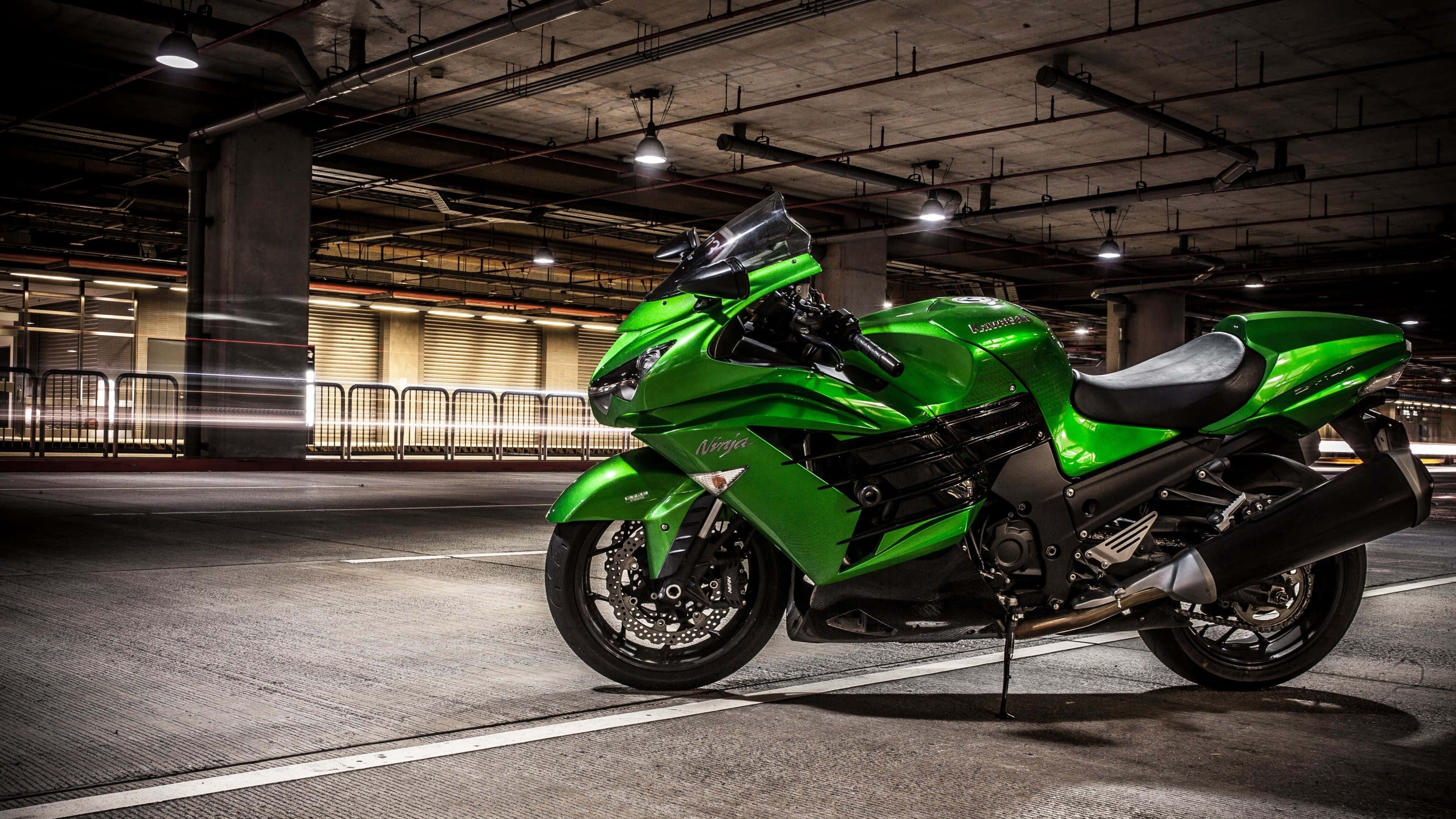 Kawasaki Desktop 桌布 壁紙 — 一輛充滿活力的綠色運動機車在光線昏暗的地下停車場中，於人造燈光下閃閃發光。