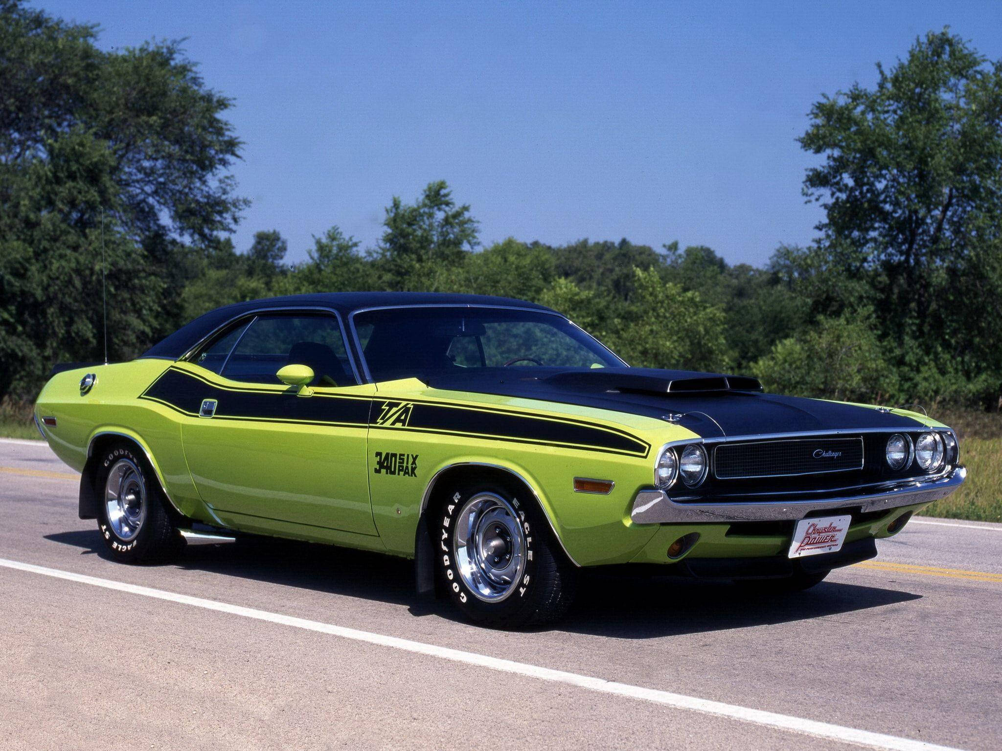 Challenger 桌布 壁紙 — 一輛充滿活力的萊姆綠色1970年道奇挑戰者，帶有黑色引擎蓋和條紋，停在陽光明媚的道路上，周圍環繞著綠樹。