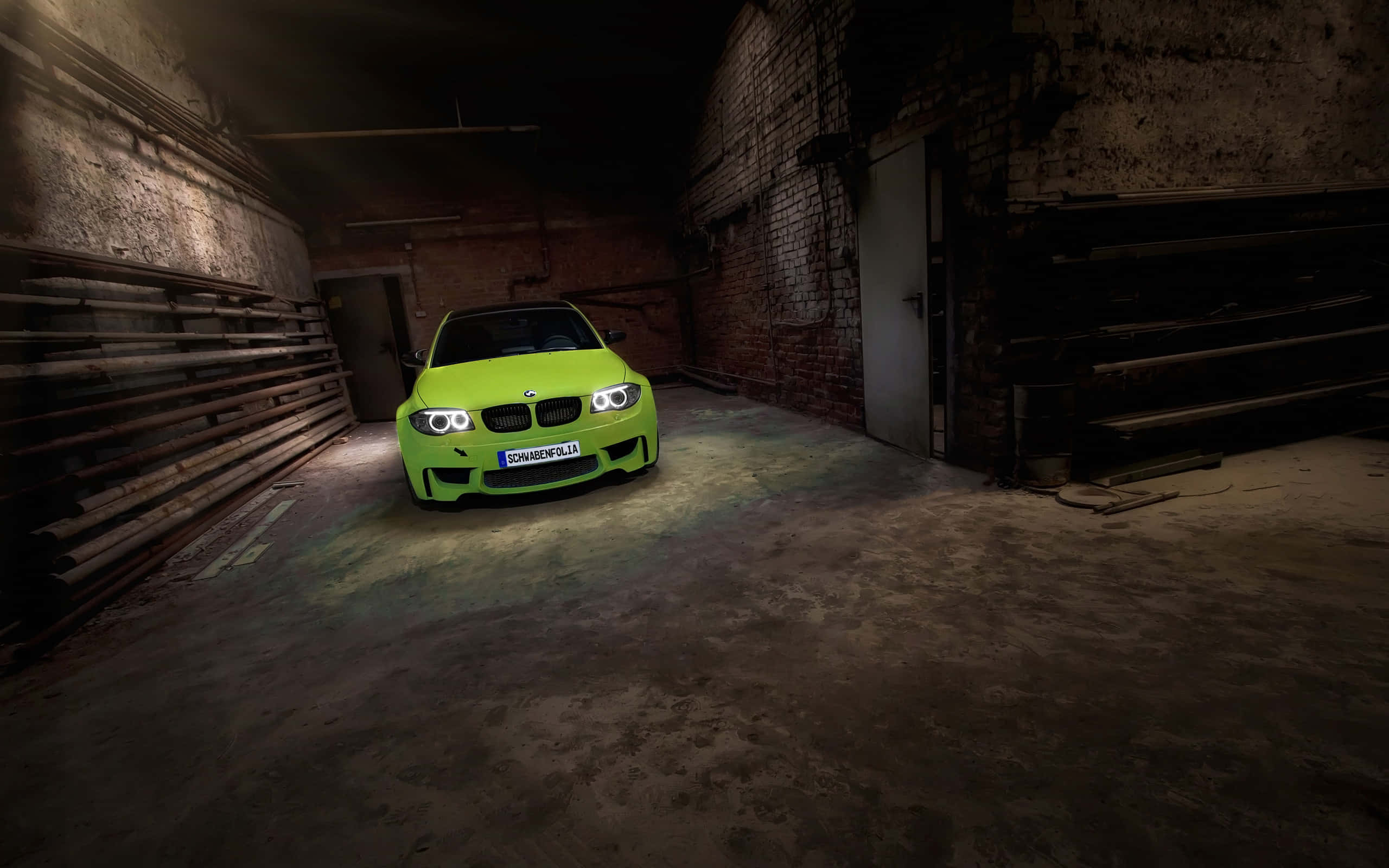 Bmw 1 Series 桌布 壁紙 — 一輛充滿活力的萊姆綠色BMW M3跑車在昏暗、粗糙的工業倉庫中，於車頭燈下閃耀。