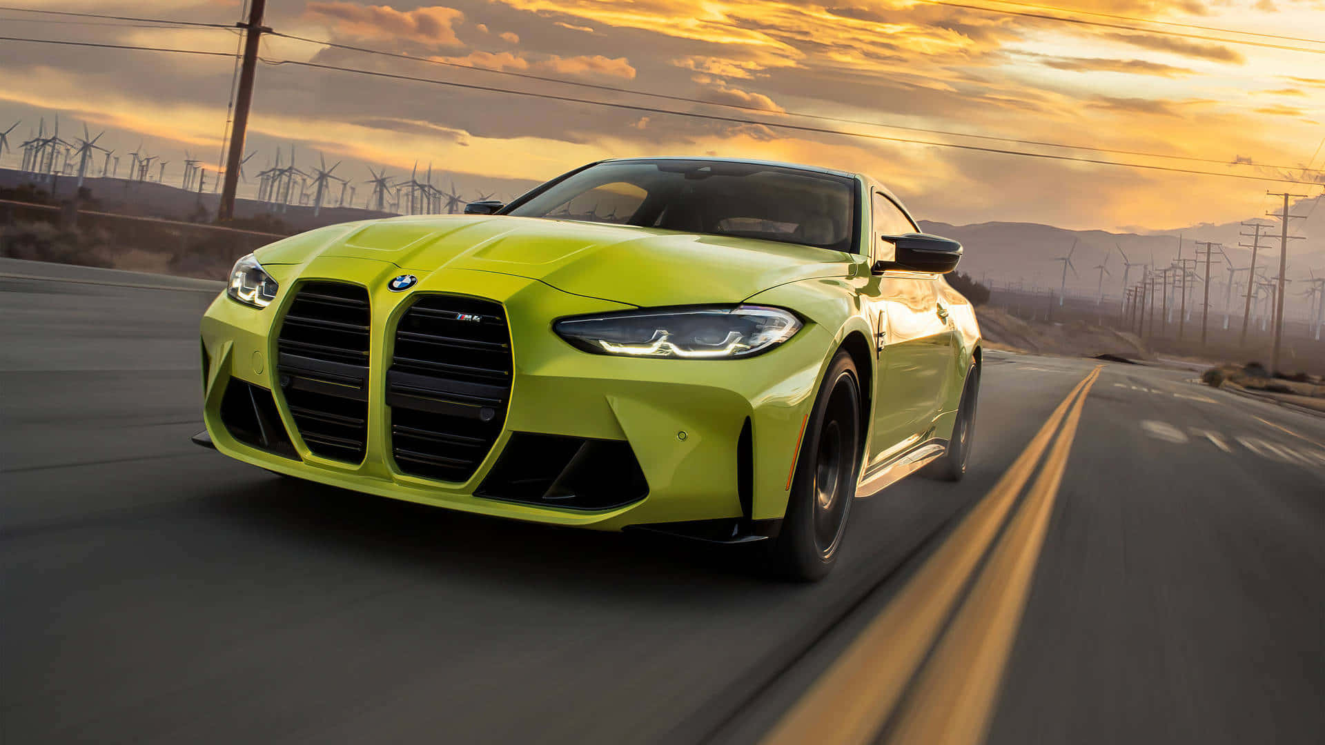 BMW 動圖 桌布 壁紙 — 一輛充滿活力的萊姆綠色BMW M4雙門跑車在日落時分沿著沙漠高速公路疾駛，遠處有風力發電機。