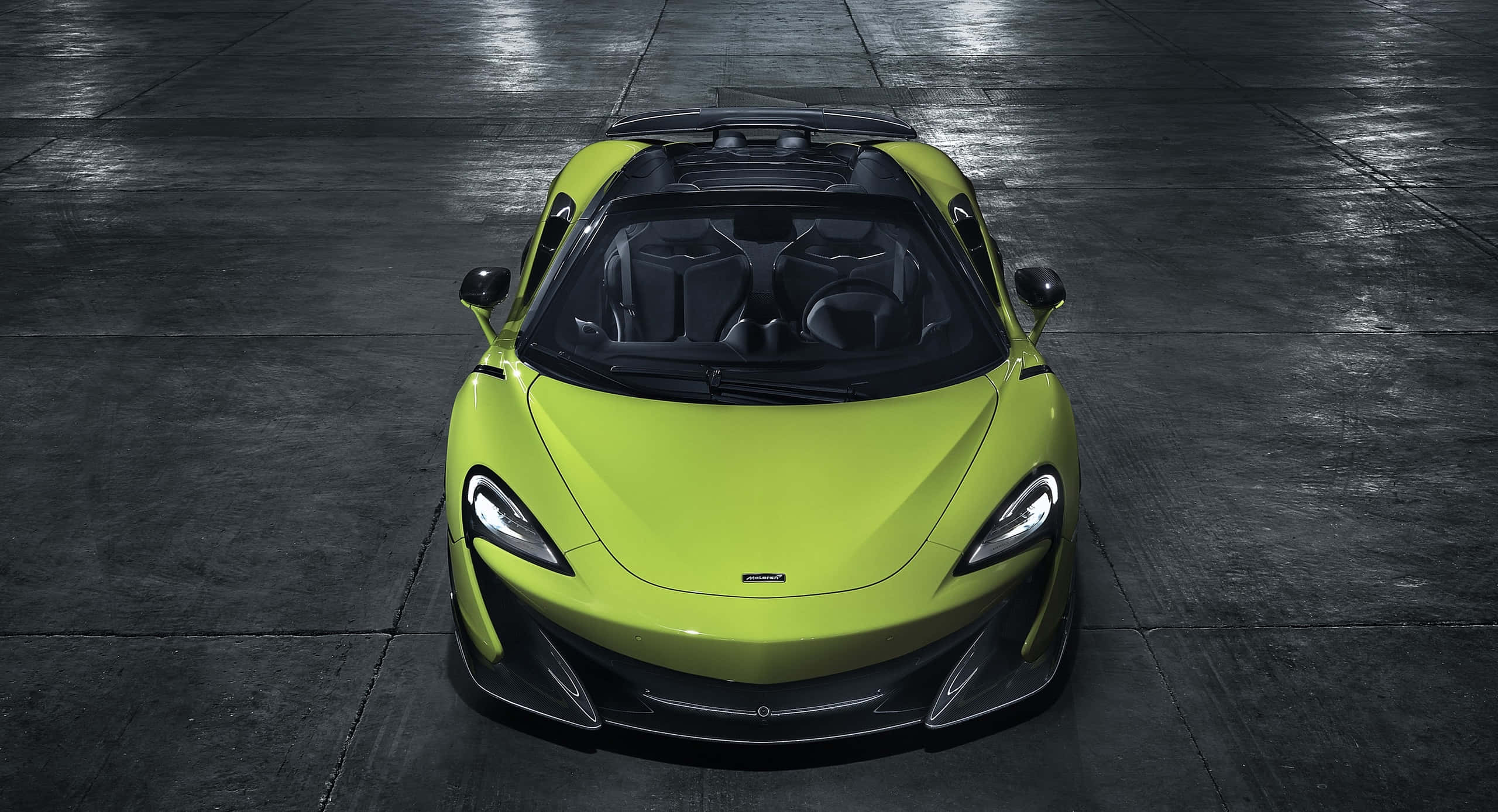 Mclaren 600lt 桌布 壁紙 — 一輛充滿活力的萊姆綠色McLaren跑車，配備黑色軟頂，在戲劇性燈光下居中停放於深色潮濕的混凝土地板上。