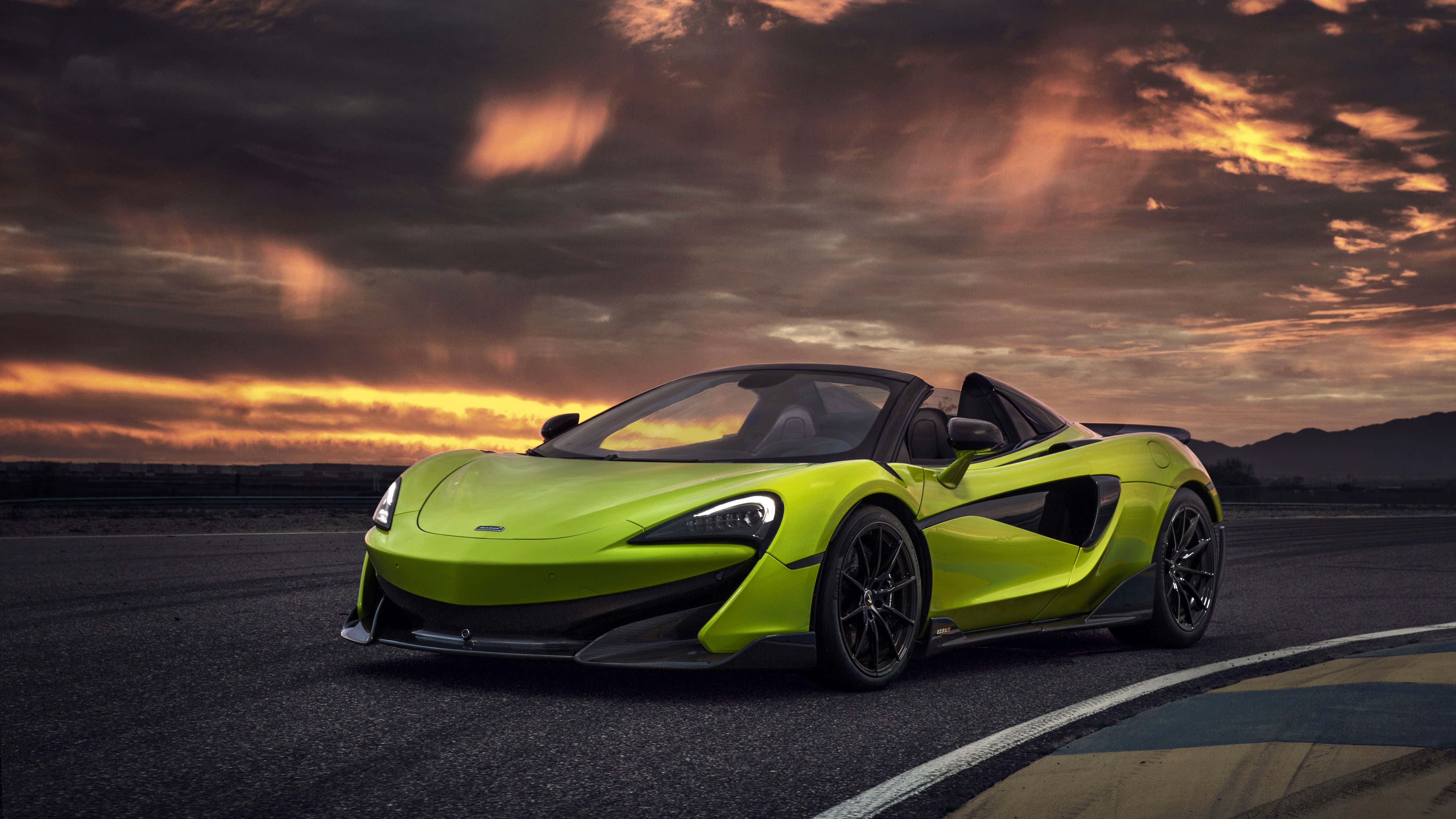 麥拉倫 桌布 壁紙 — 一輛充滿活力的萊姆綠色McLaren跑車停放在賽道上，背景是壯麗的日落天空，帶有火紅橙色的雲彩。