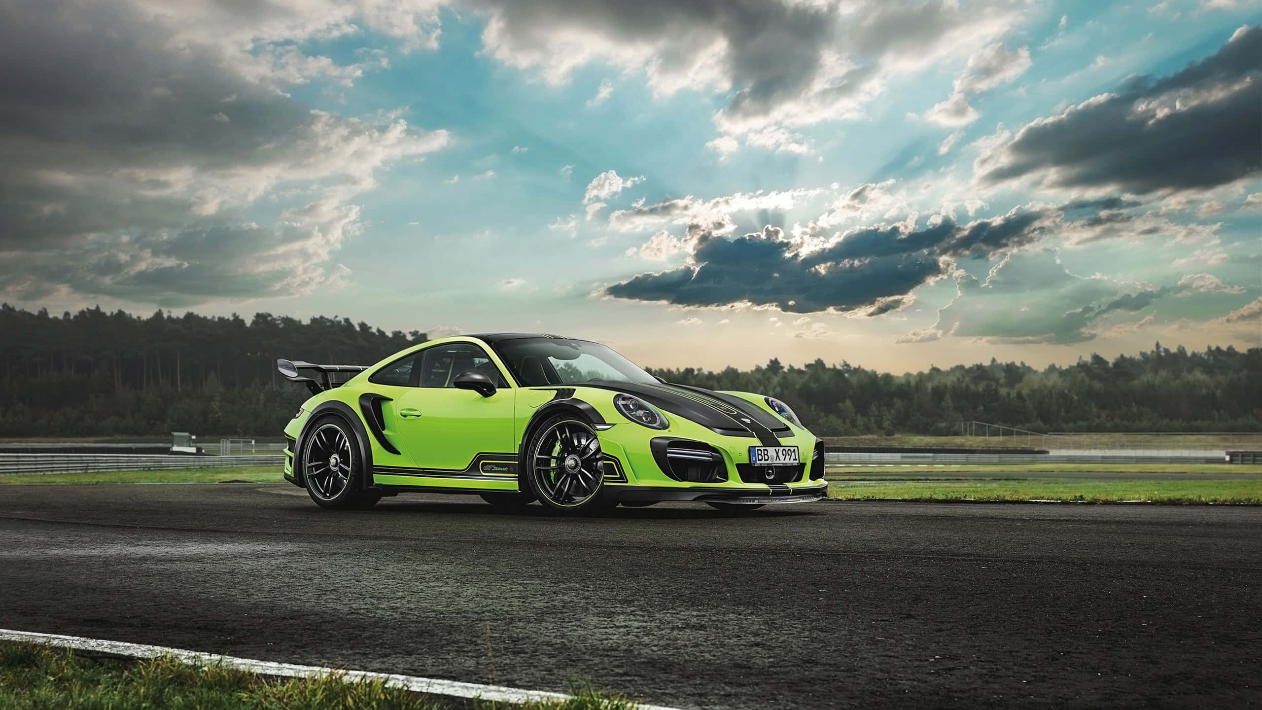 保時捷 桌布 壁紙 — 一輛充滿活力的萊姆綠色保時捷911 GT2 RS，帶有黑色點綴，在戲劇性的多雲天空下，停在潮濕的賽道上。
