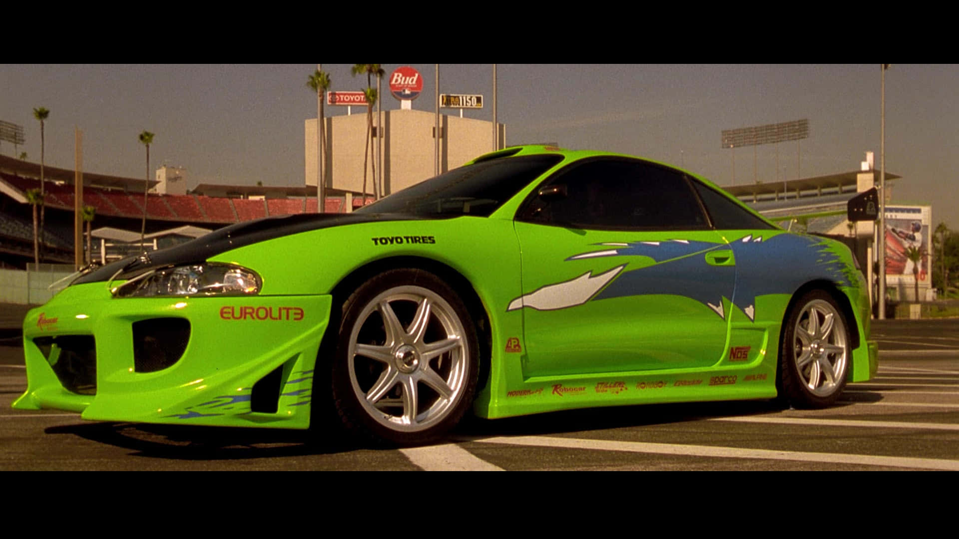 Fast And Furious 1 桌布 壁紙 — 一輛充滿活力的萊姆綠色改裝跑車，帶有藍色和白色圖案，停泊在朦朧天空下的賽道上。
