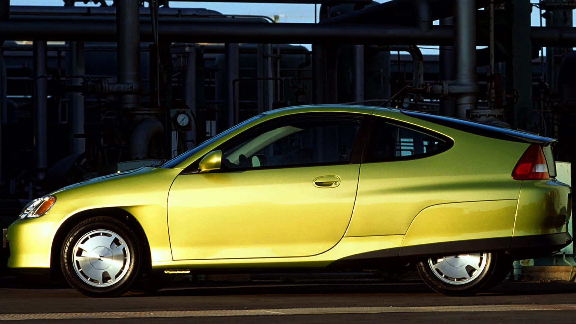Honda Insight 桌布 壁紙 — 一輛充滿活力的萊姆綠色混合動力跑車在明亮的日光下停放在工業管道旁邊。