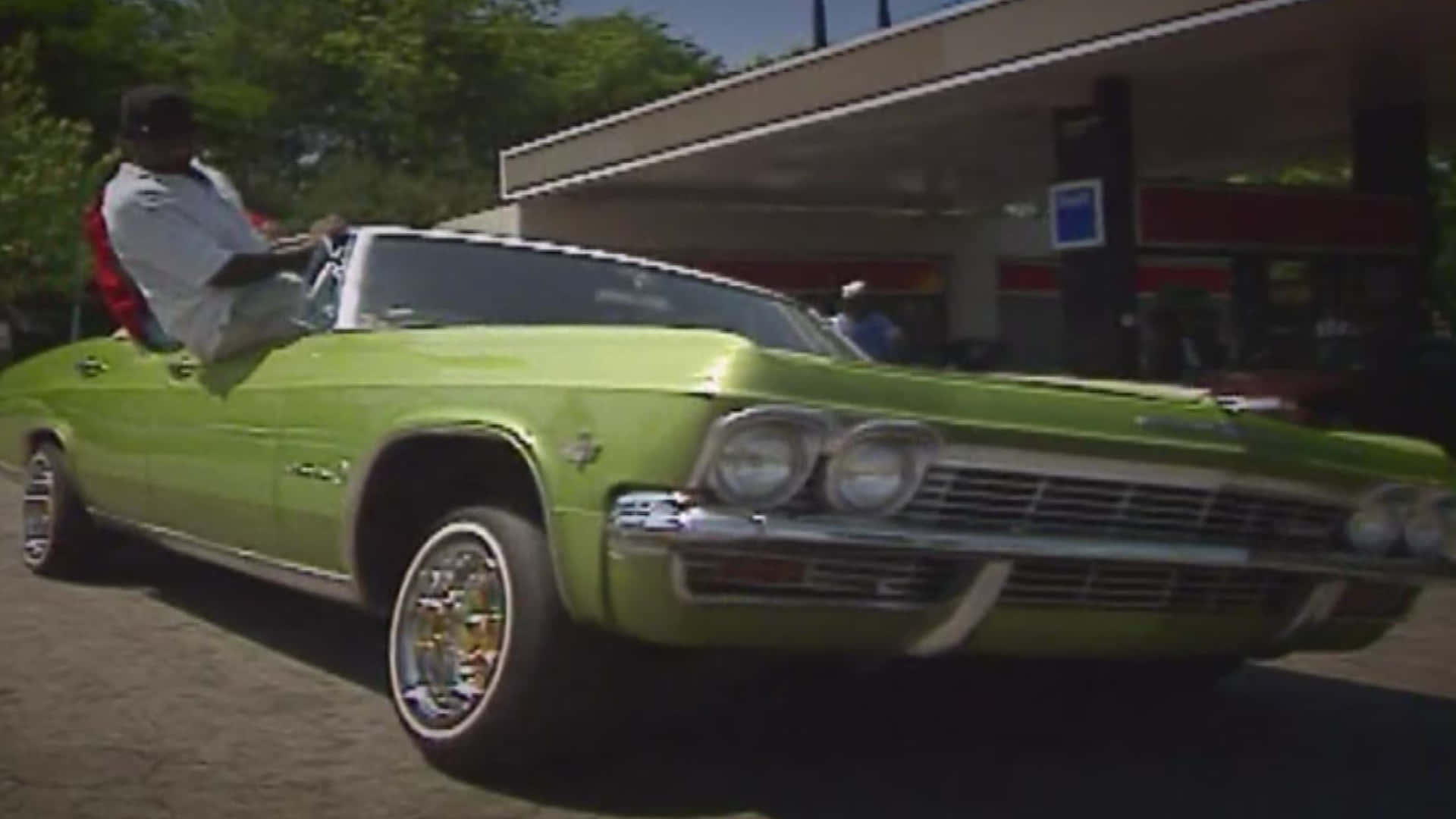Freaknik 90s 桌布 壁紙 — 一輛充滿活力的萊姆綠色經典敞篷車停在加油站，駕駛座上坐著一名男子。