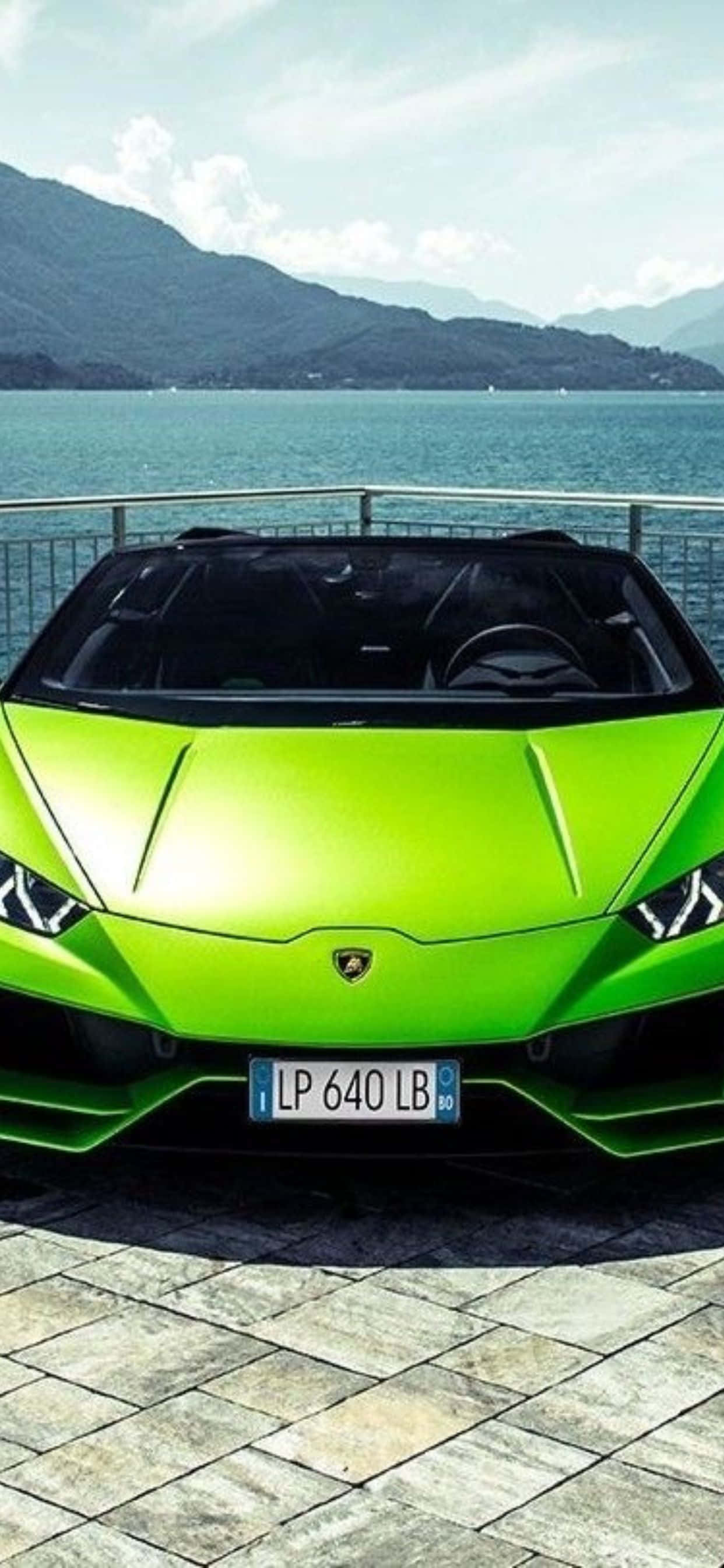 Lamborghini Phone 桌布 壁紙 — 一輛充滿活力的萊姆綠色藍寶堅尼跑車停泊在石碼頭上，俯瞰著遠處有山巒的平靜藍色大海。