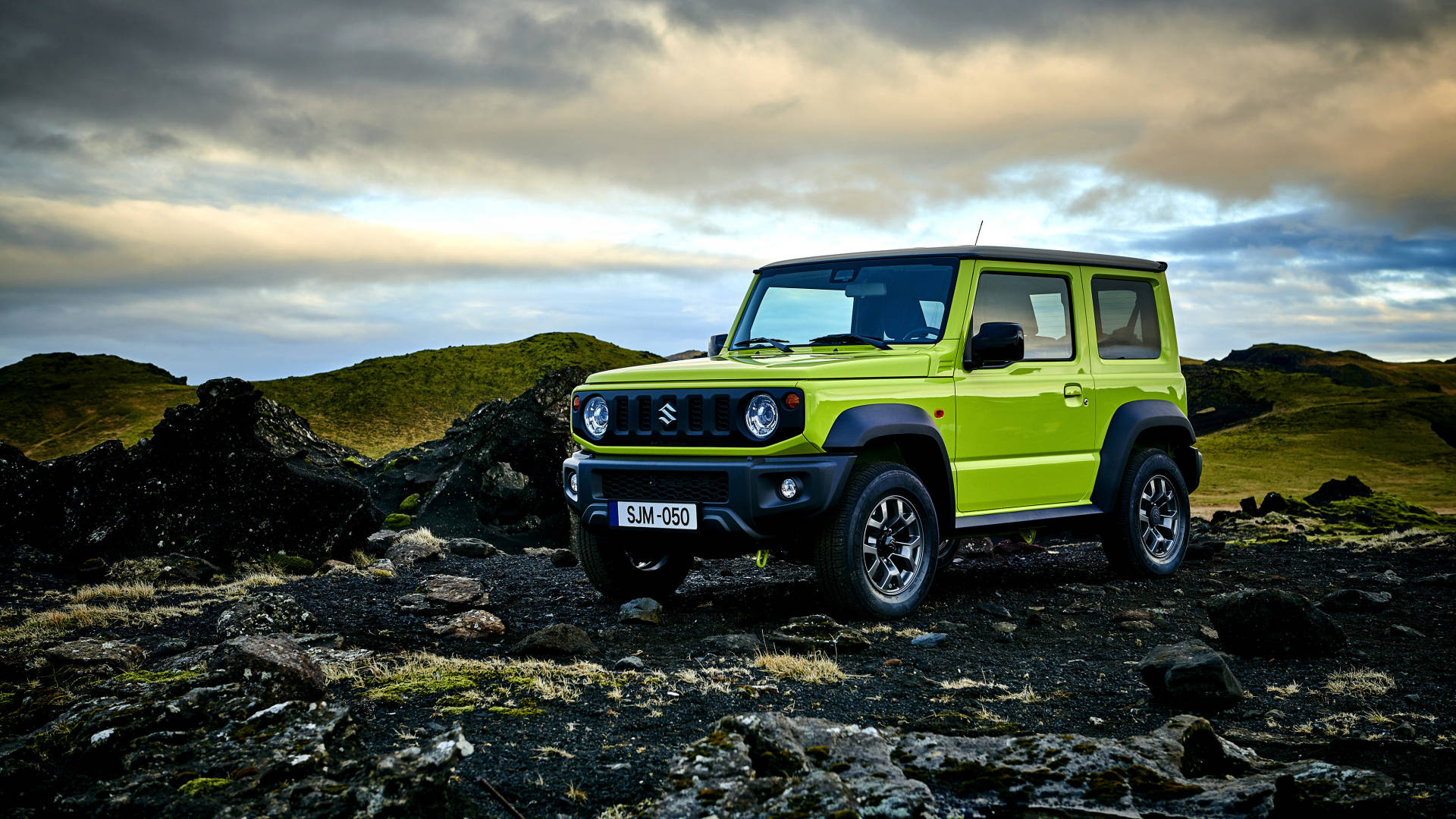 Suzuki 桌布 壁紙 — 一輛充滿活力的萊姆綠色鈴木 Jimny 在崎嶇的火山地形上，在陰鬱的暮色天空下傲然矗立。