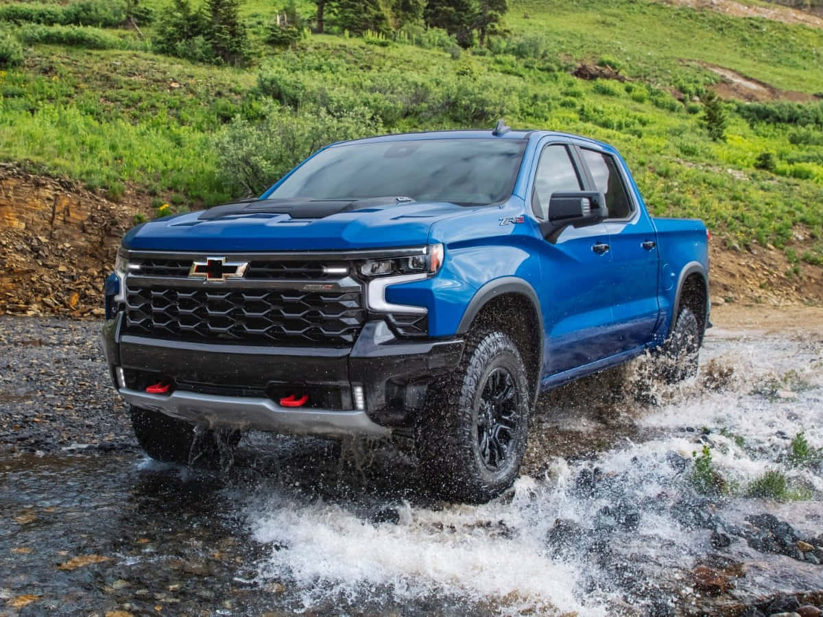 雪佛蘭 桌布 壁紙 — 一輛充滿活力的藍色 Chevrolet Silverado 卡車在茂密的綠色山地地形中濺起水花穿過岩石溪流。