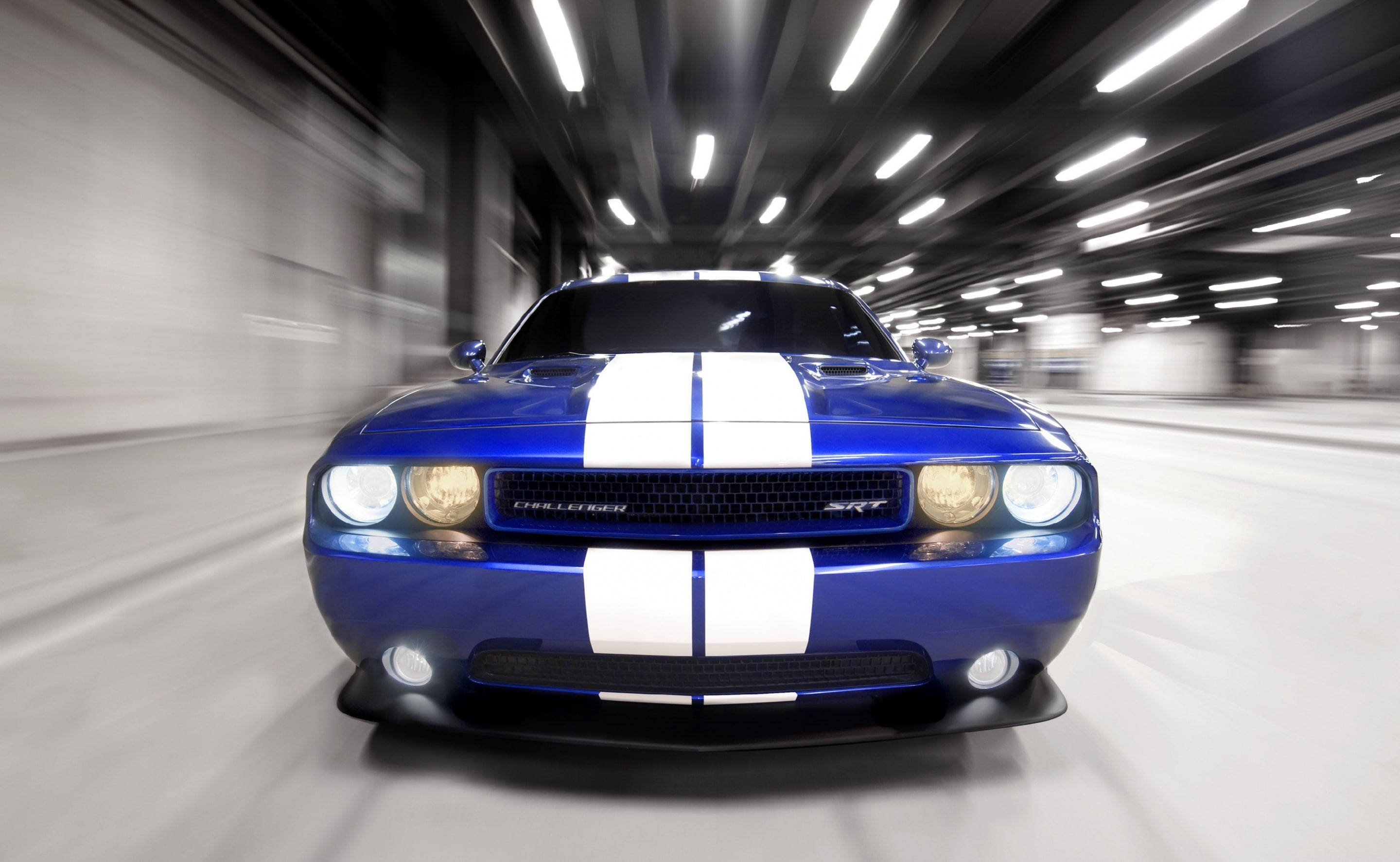 race 桌布 壁紙 — 一輛充滿活力的藍色 Dodge Challenger SRT 帶有白色賽車條紋，在隧道中疾馳，留下動態模糊的痕跡。