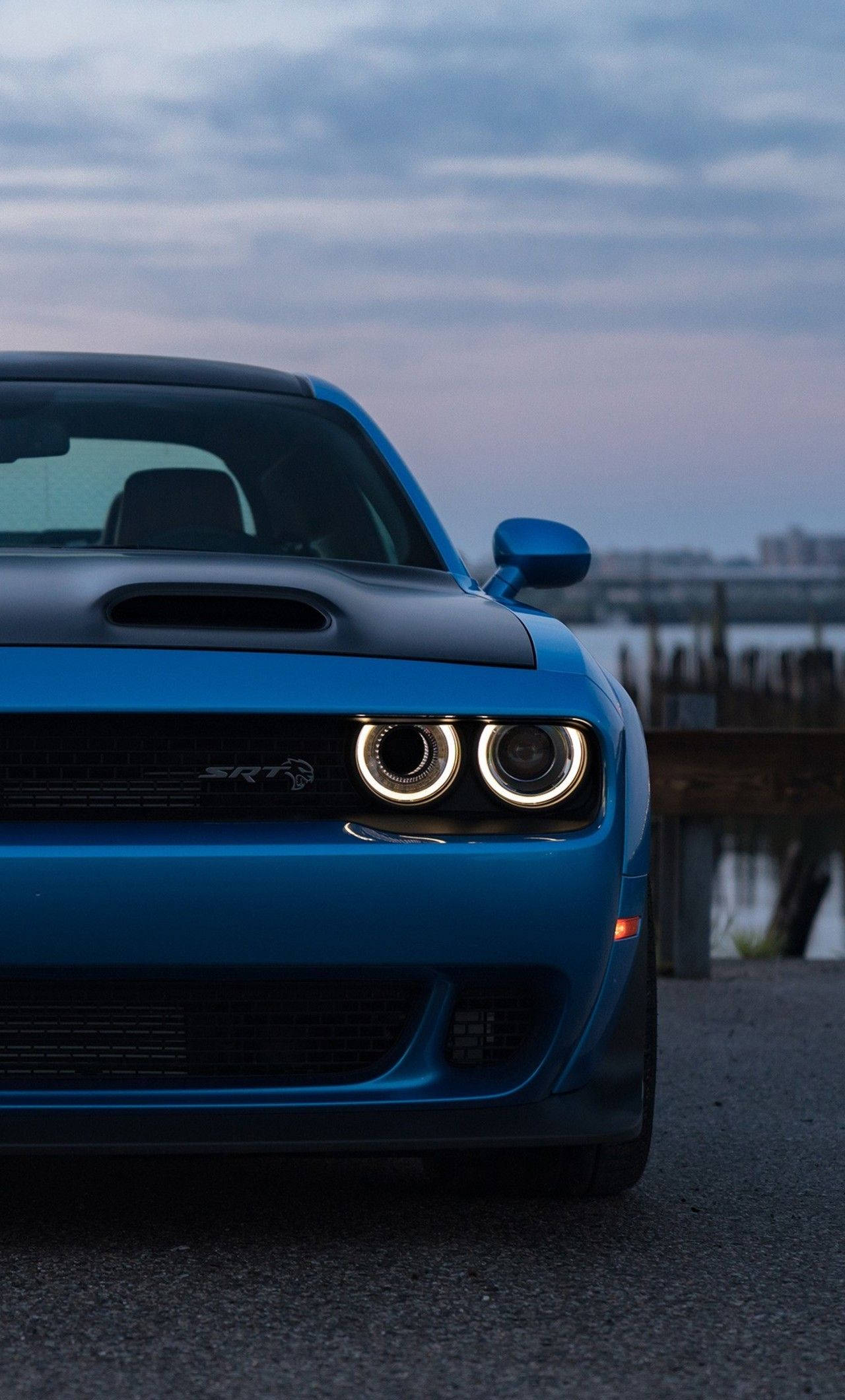 Challenger 桌布 壁紙 — 一輛充滿活力的藍色 Dodge Challenger SRT Hellcat 在黃昏時停車，圓形車頭燈在陰雲密布的天空下發光。