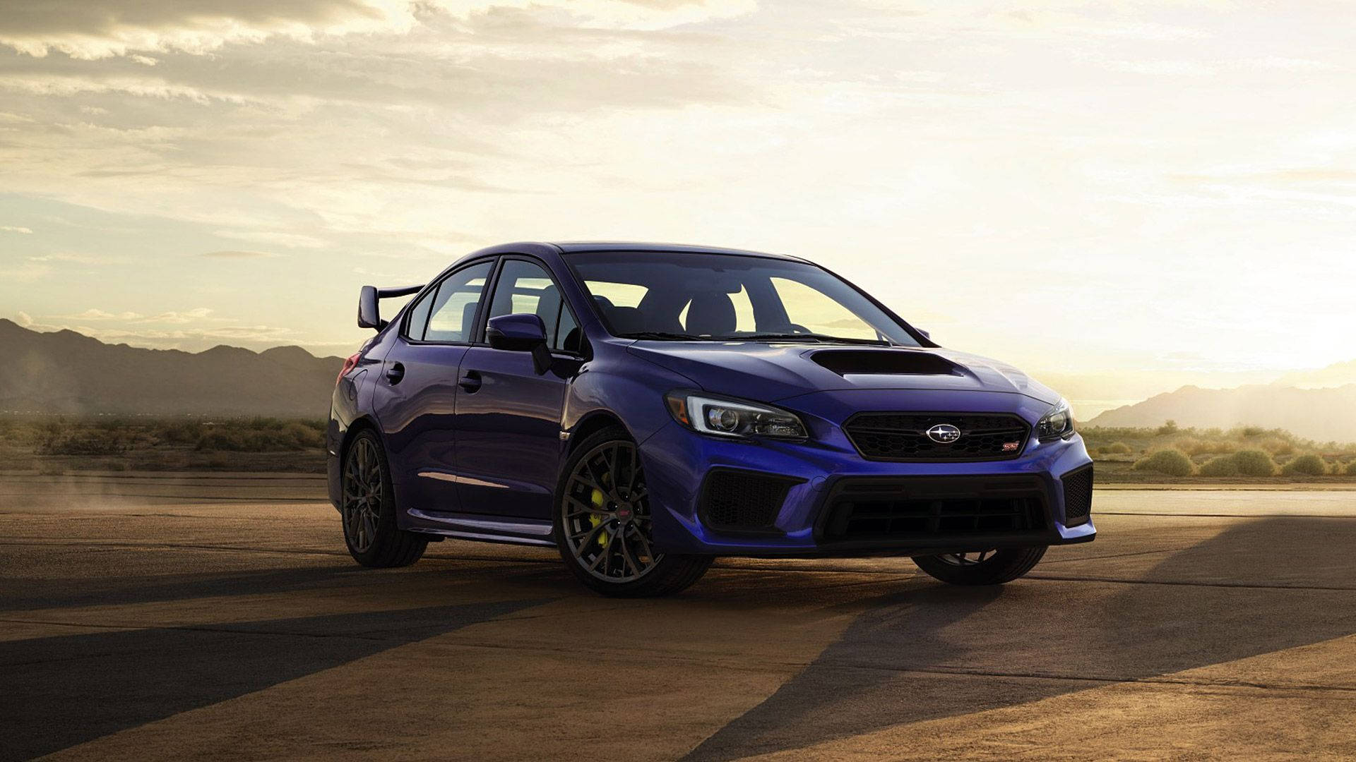 昴 桌布 壁紙 — 一輛充滿活力的藍色 Subaru WRX STI 跑車停泊在沙漠賽道上，背景是山脈，正值黃金時刻。