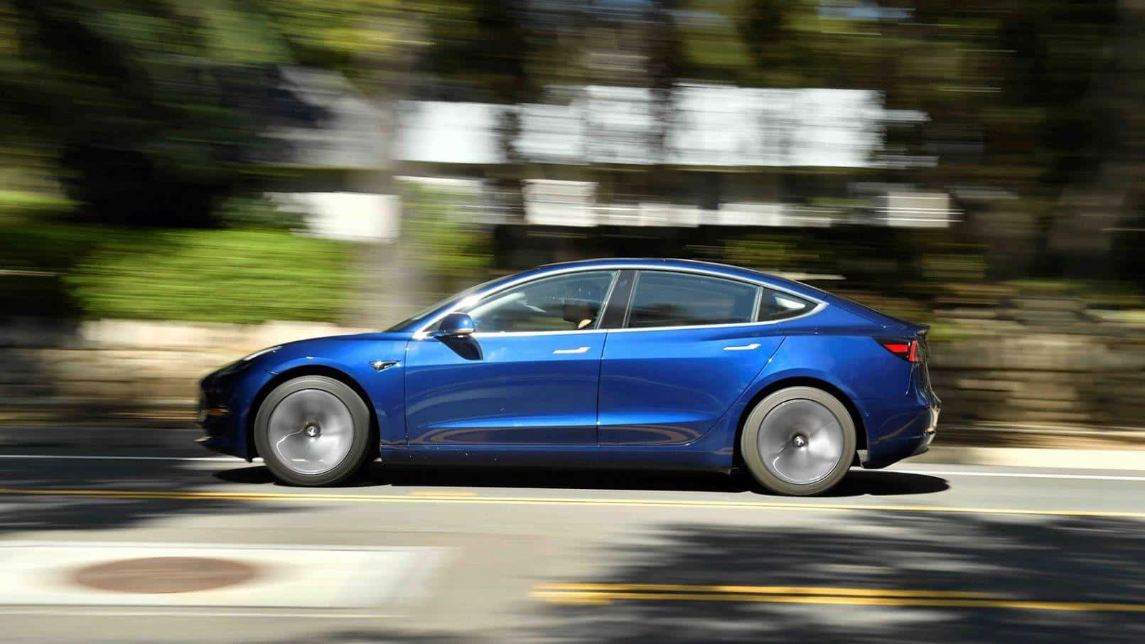 Tesla Model 3 桌布 壁紙 — 一輛充滿活力的藍色 Tesla Model 3 在陽光明媚的道路上行駛，模糊的綠色植物飛馳而過。