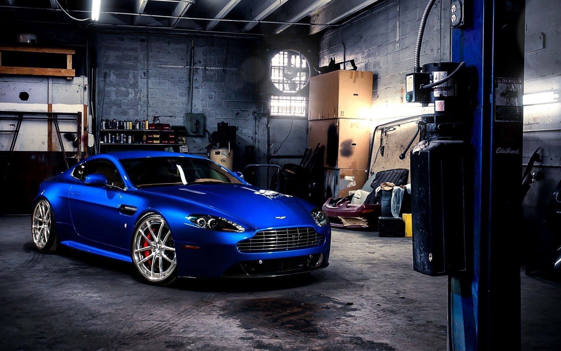 Garage 桌布 壁紙 — 一輛充滿活力的藍色Aston Martin跑車在刺眼的車庫燈光下閃閃發光，周圍散落著工具和設備。