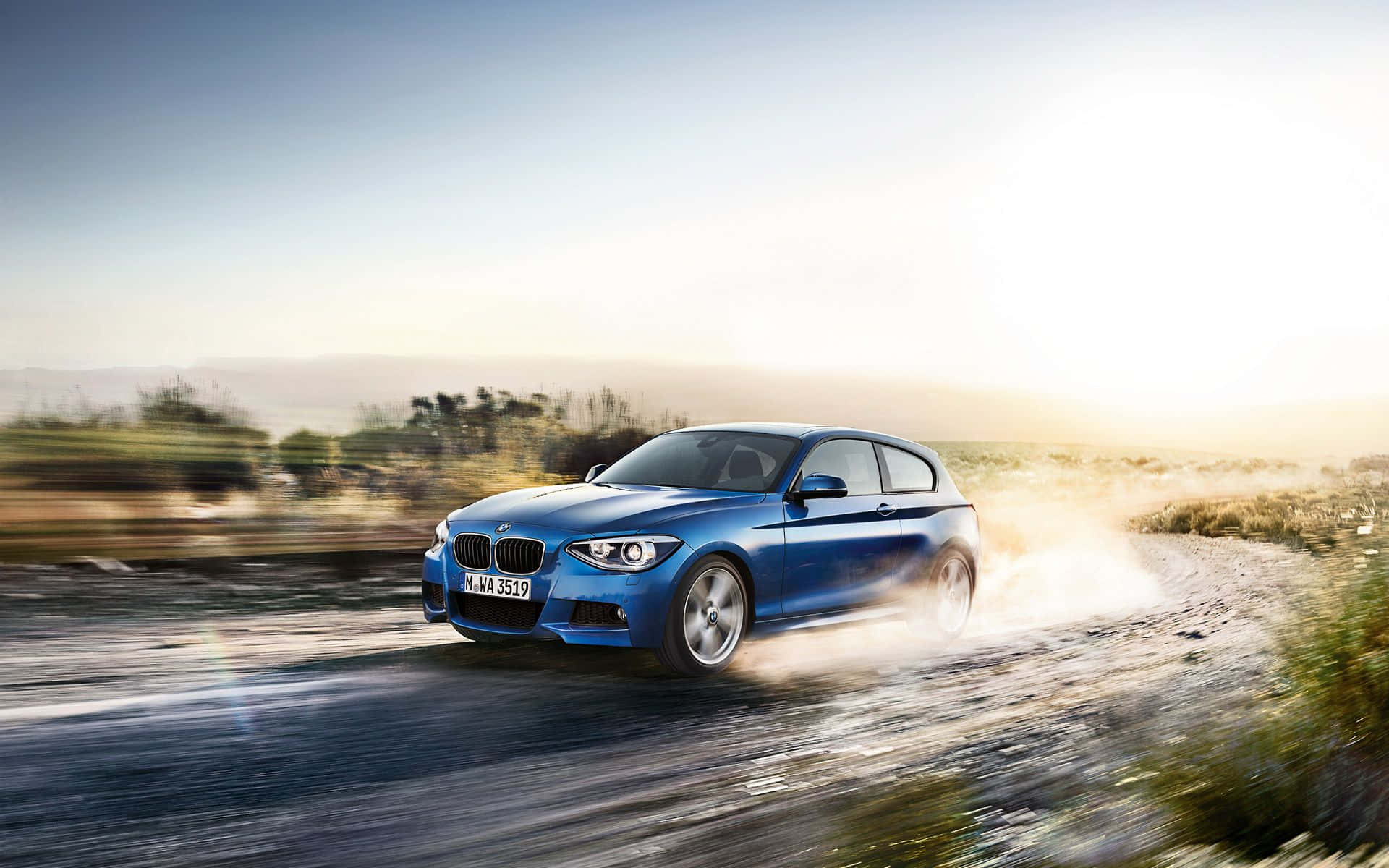 Bmw 1 Series 桌布 壁紙 — 一輛充滿活力的藍色BMW 1系列在塵土飛揚的鄉村道路上疾馳，在明亮的金色天空下揚起碎石。