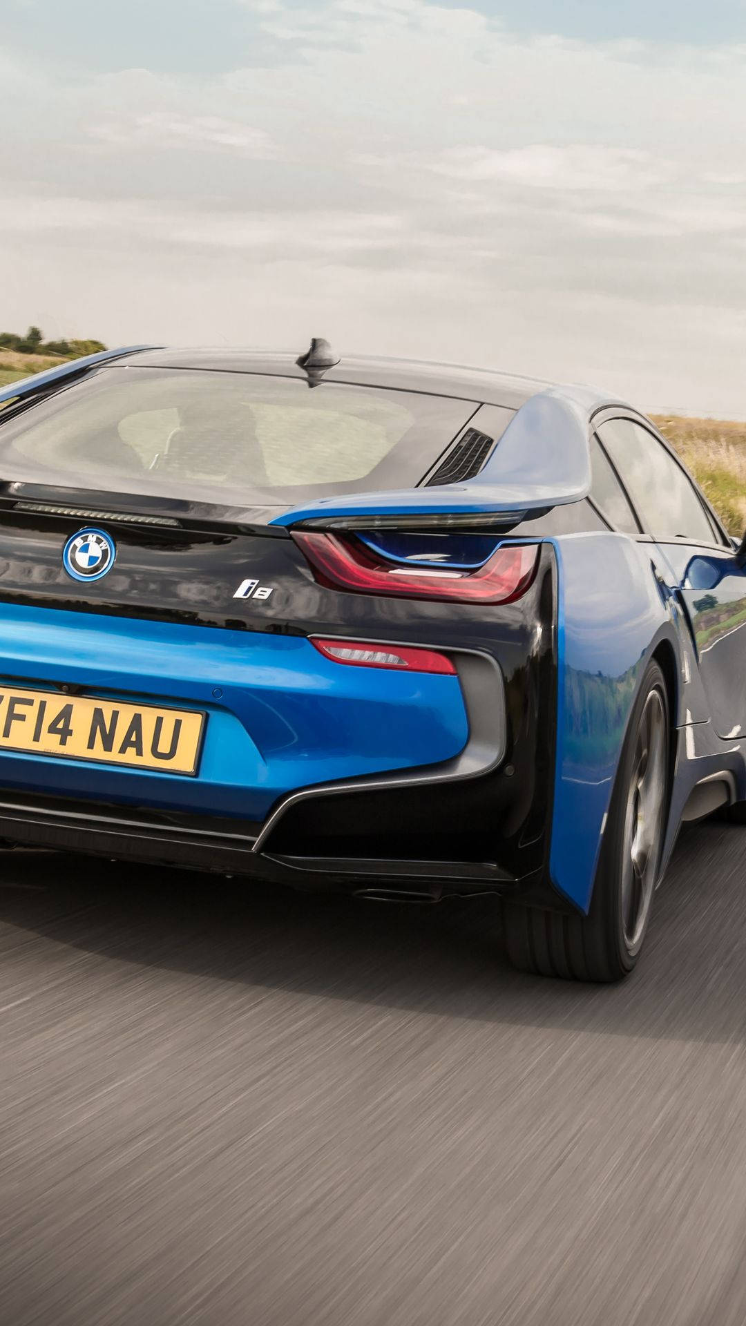 X 桌布 壁紙 — 一輛充滿活力的藍色BMW i8跑車在陰天下行駛在鄉村道路上，動態模糊強調了其動態運動。