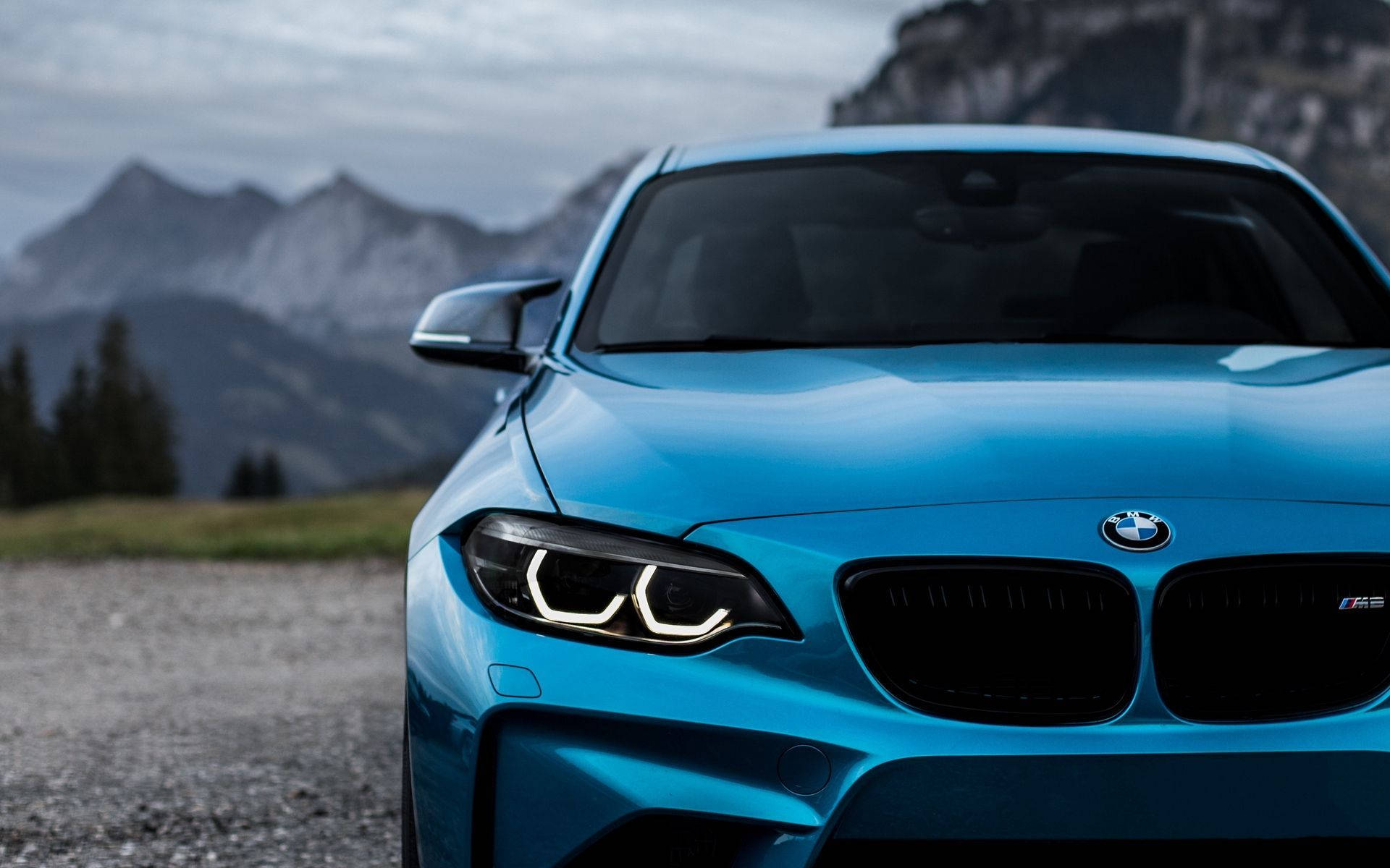 BMW 動圖 桌布 壁紙 — 一輛充滿活力的藍色BMW M2跑車停泊在碎石路上，背景是霧氣籠罩的山巒。