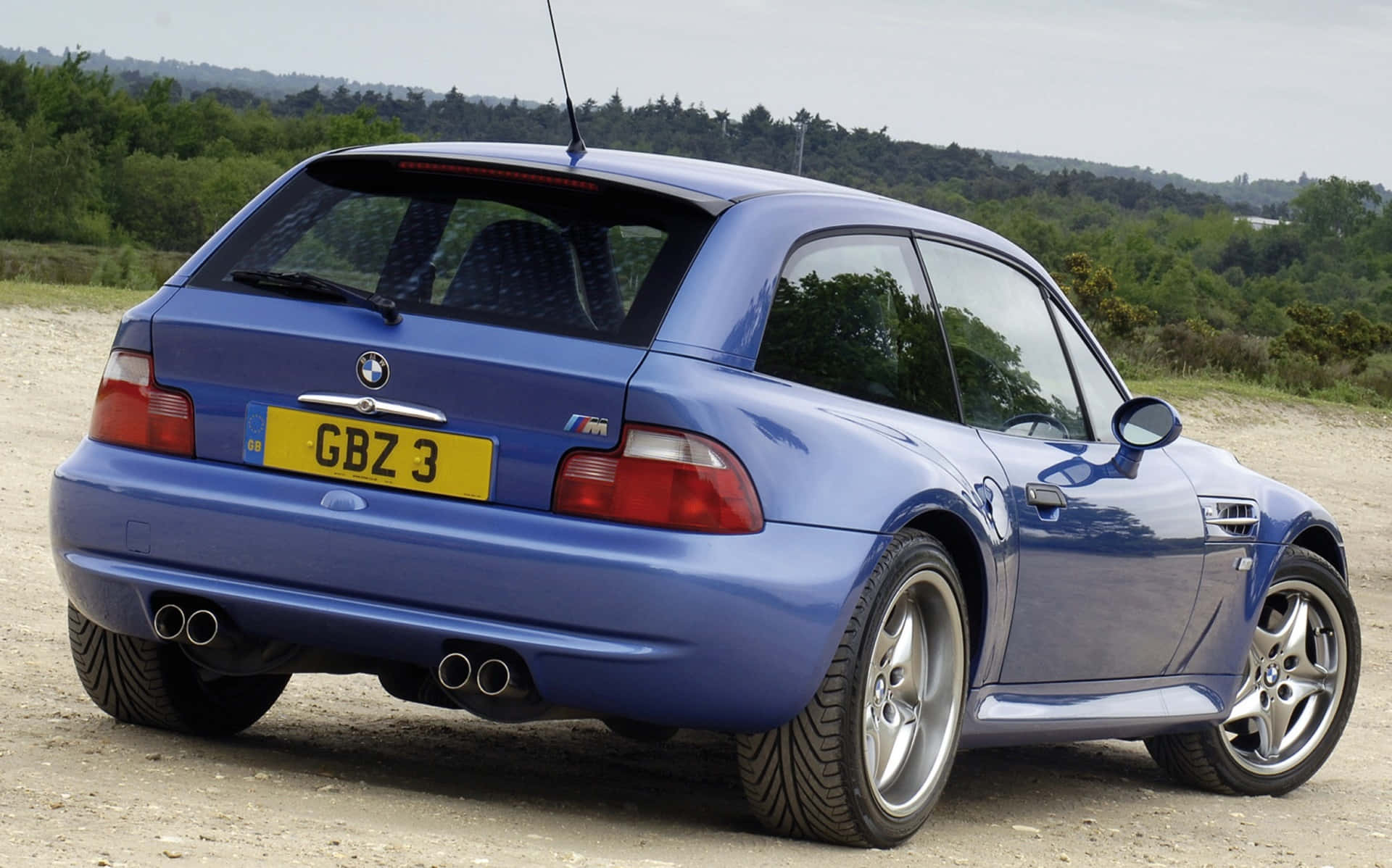 Bmw Z3 桌布 壁紙 — 一輛充滿活力的藍色BMW M3跑車停在碎石路上，背景是綠色的山丘。