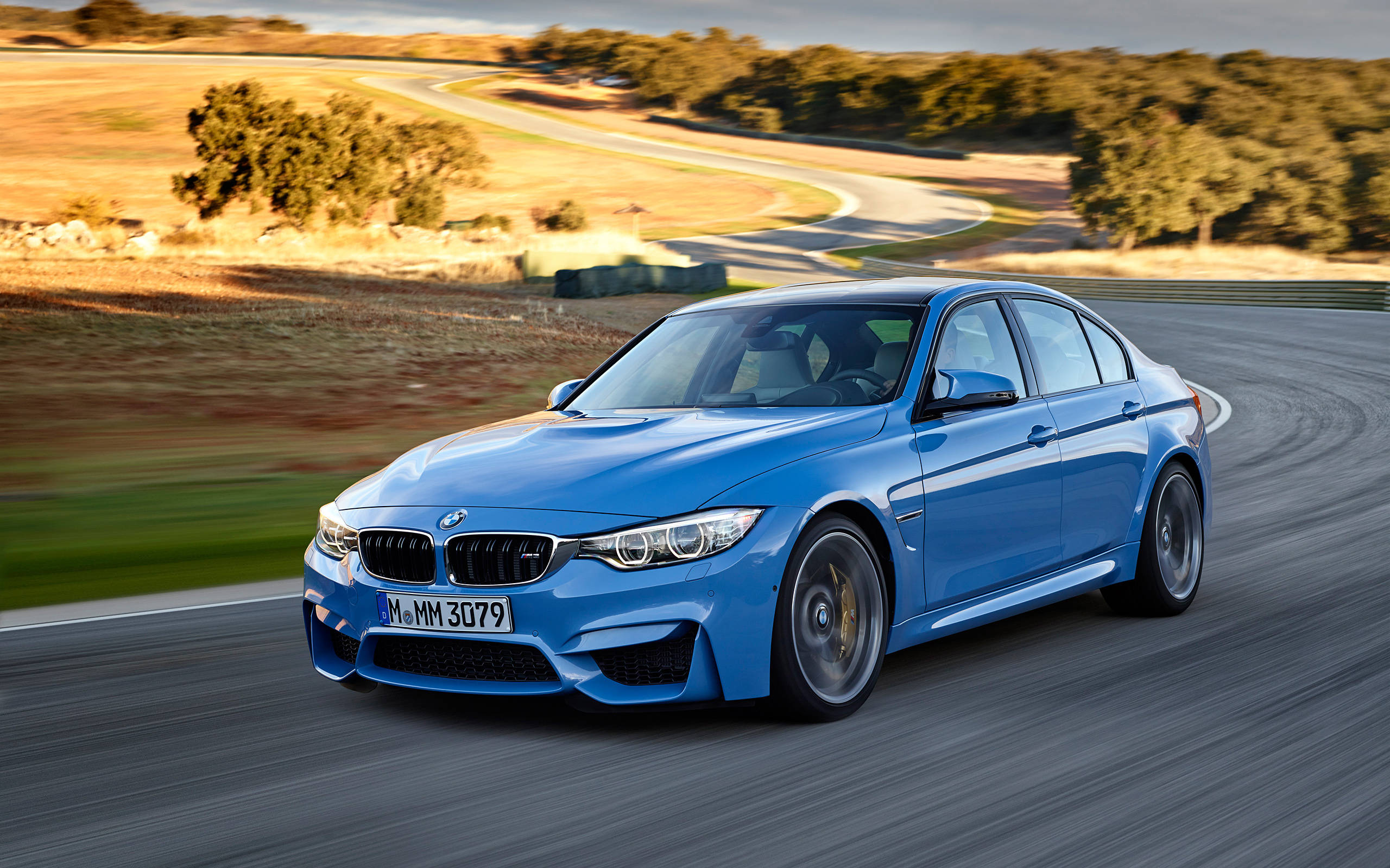 BMW 動圖 桌布 壁紙 — 一輛充滿活力的藍色BMW M3轎車沿著蜿蜒的瀝青道路穿過陽光明媚的鄉村風景飛馳。