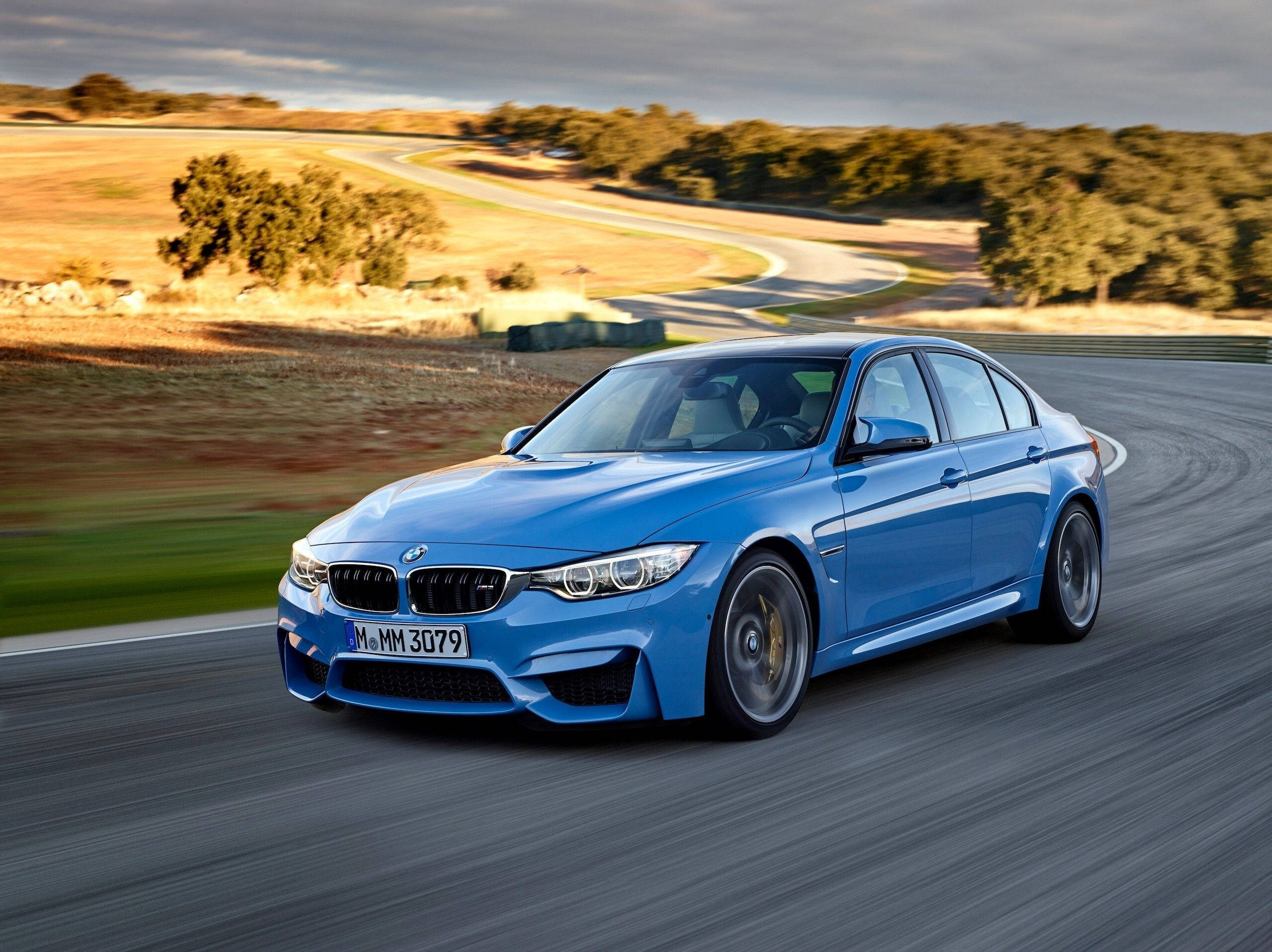 BMW 動圖 桌布 壁紙 — 一輛充滿活力的藍色BMW M3轎車在陰天下行駛在蜿蜒的鄉村道路上。