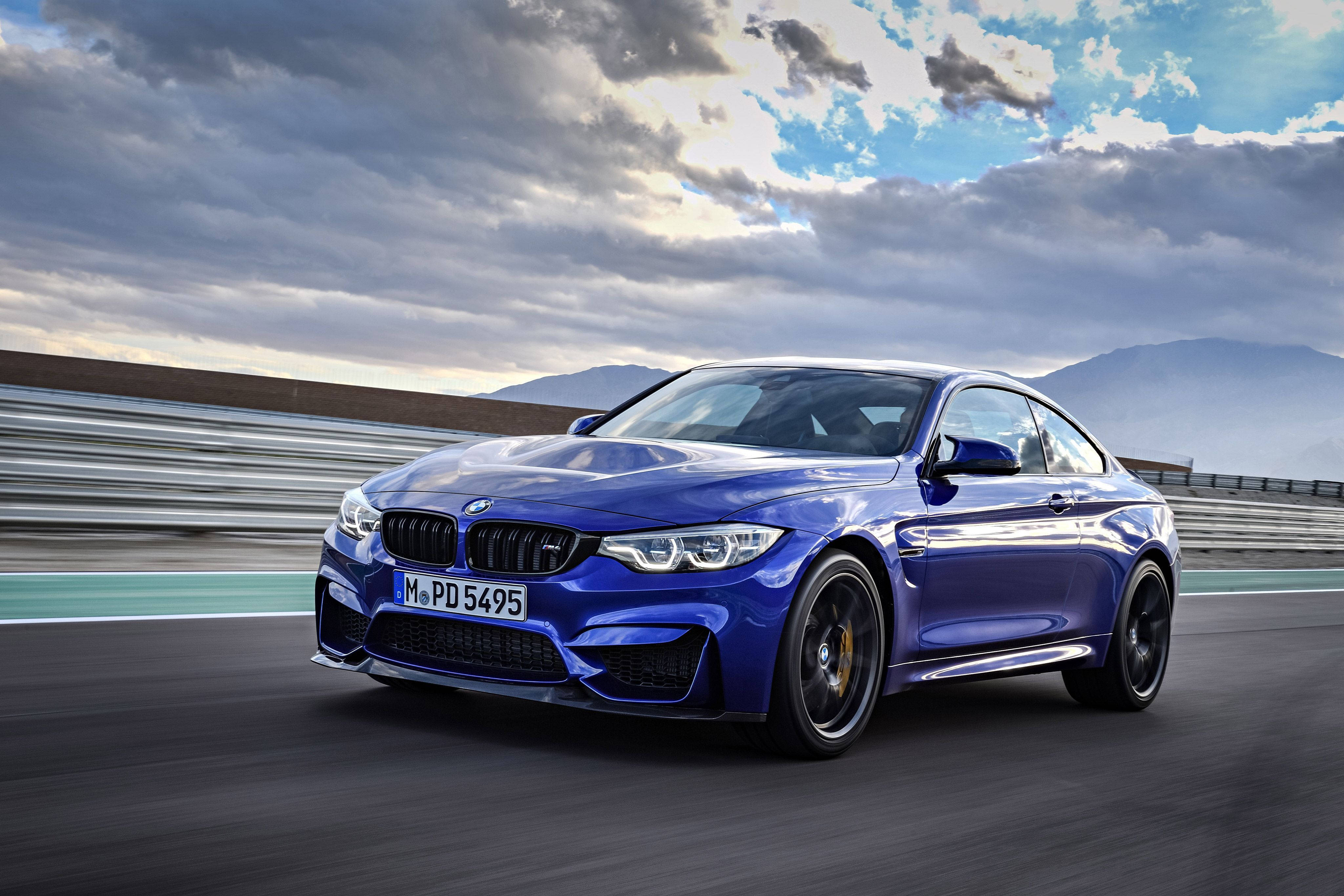 藍色 桌布 壁紙 — 一輛充滿活力的藍色BMW M4 Coupe在戲劇性的多雲天空和遠處山脈下沿著賽道飛馳。