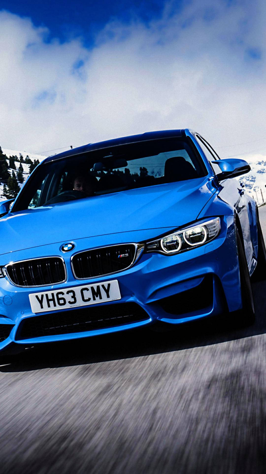 X 桌布 壁紙 — 一輛充滿活力的藍色BMW M4在晴朗藍天和蓬鬆白雲下，沿著積雪的山路飛馳。