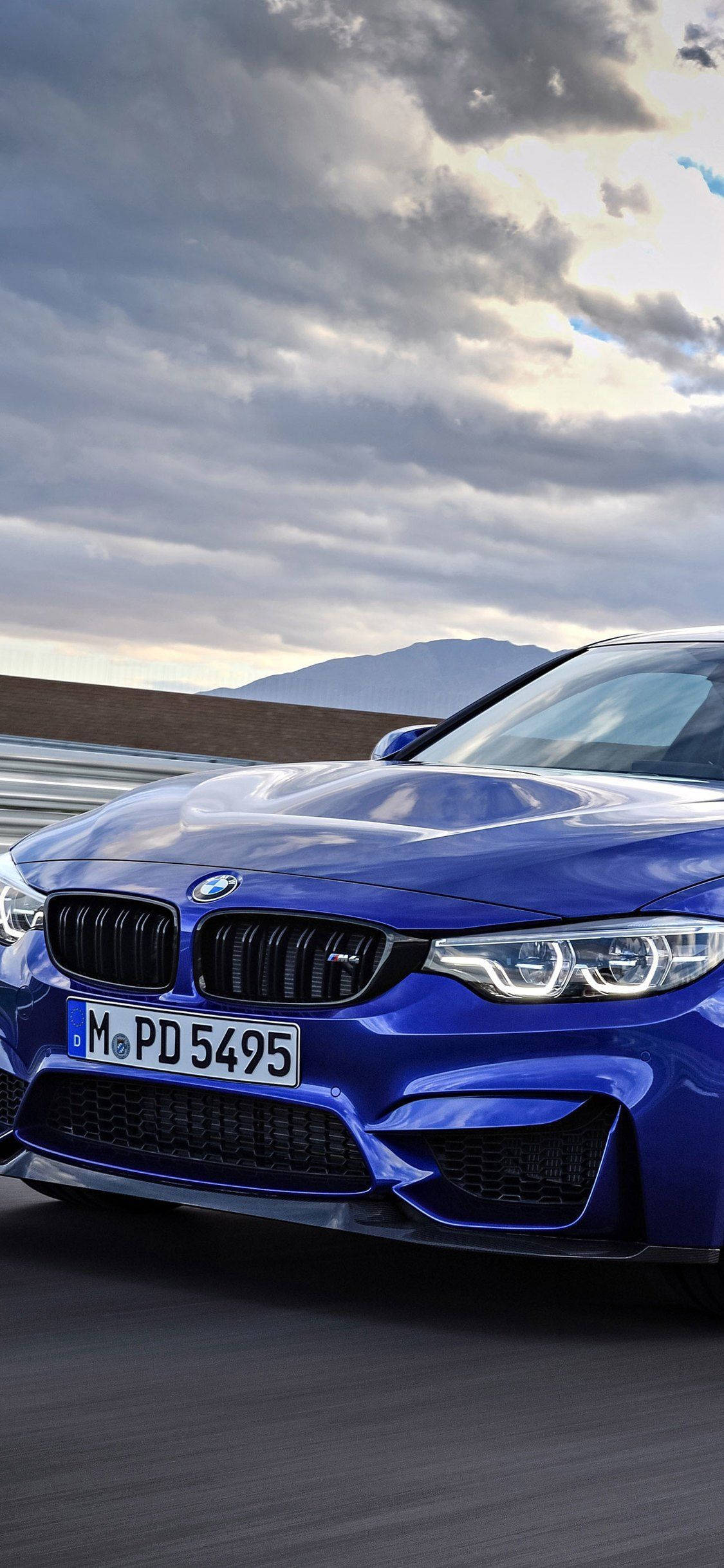 X 桌布 壁紙 — 一輛充滿活力的藍色BMW M4跑車在戲劇性的多雲天空下沿著蜿蜒的山路疾馳。