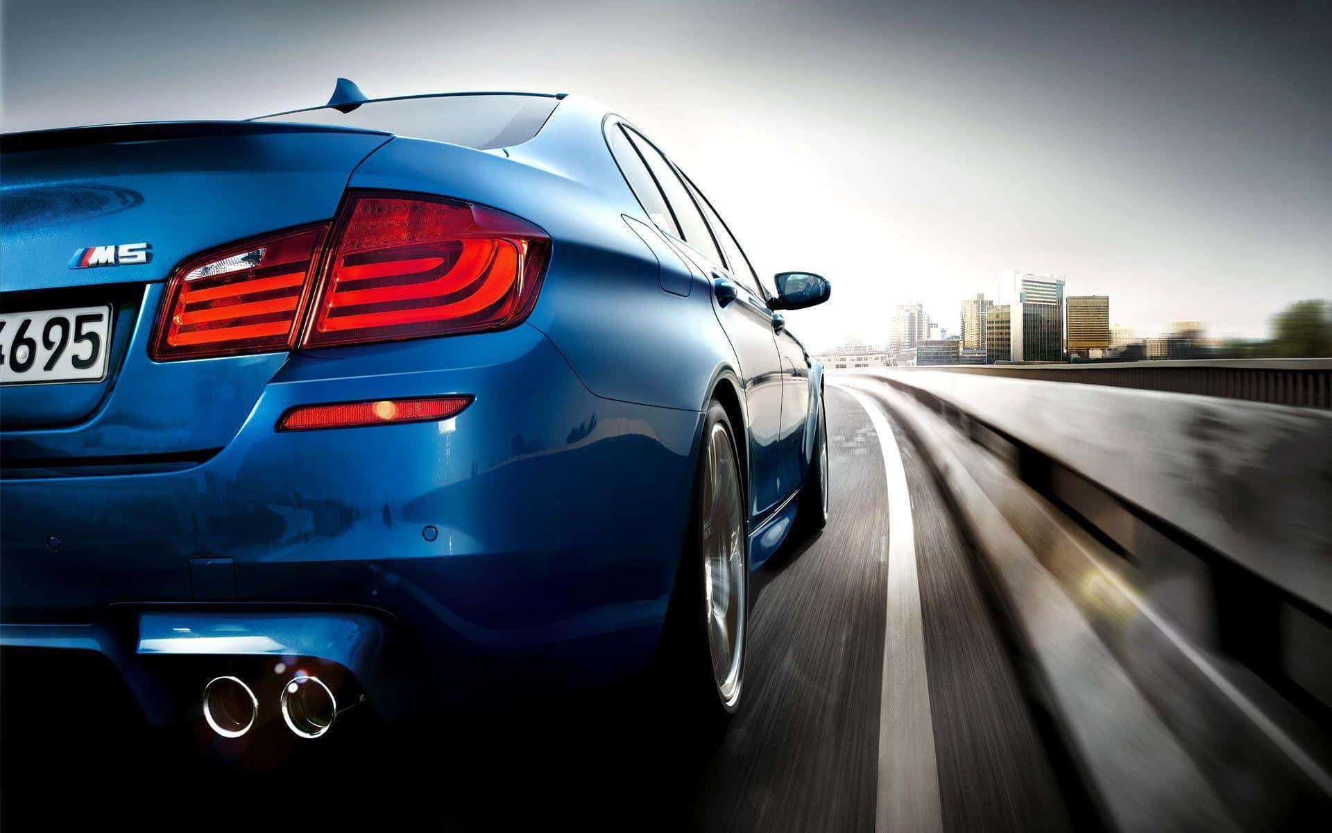 BMW 動圖 桌布 壁紙 — 一輛充滿活力的藍色BMW M5跑車在高速公路上疾馳，帶有動態模糊，遠處朦朧的城市天際線清晰可見。