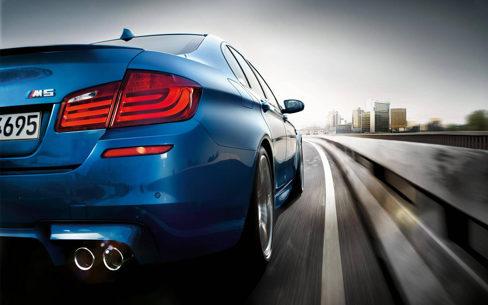 cars 桌布 壁紙 — 一輛充滿活力的藍色BMW M5跑車在高速公路上飛馳，遠處是模糊的城市天際線。