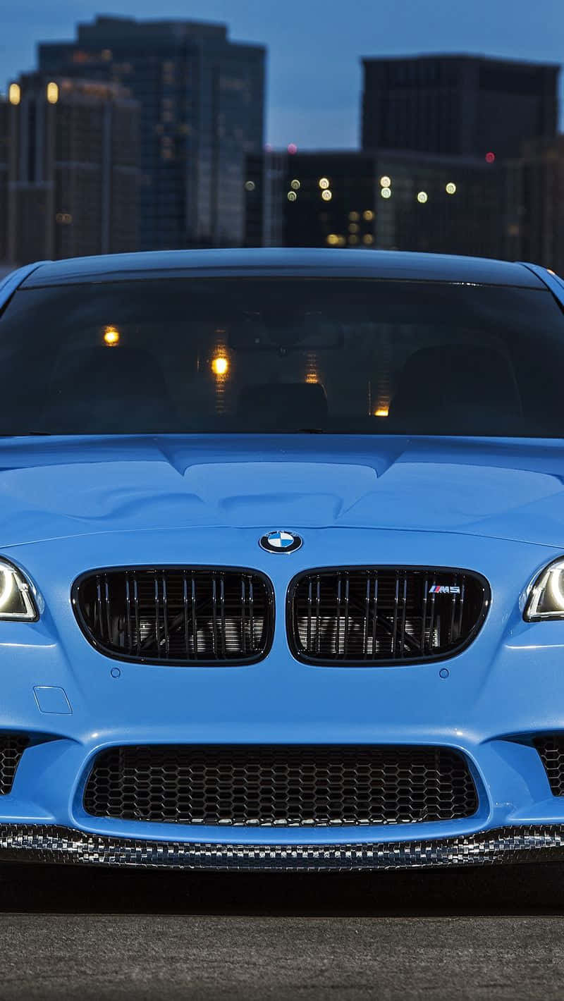 Bmw iPhone 桌布 壁紙 — 一輛充滿活力的藍色BMW M5跑車佔據前景，背後是黃昏時分閃爍的城市天際線。