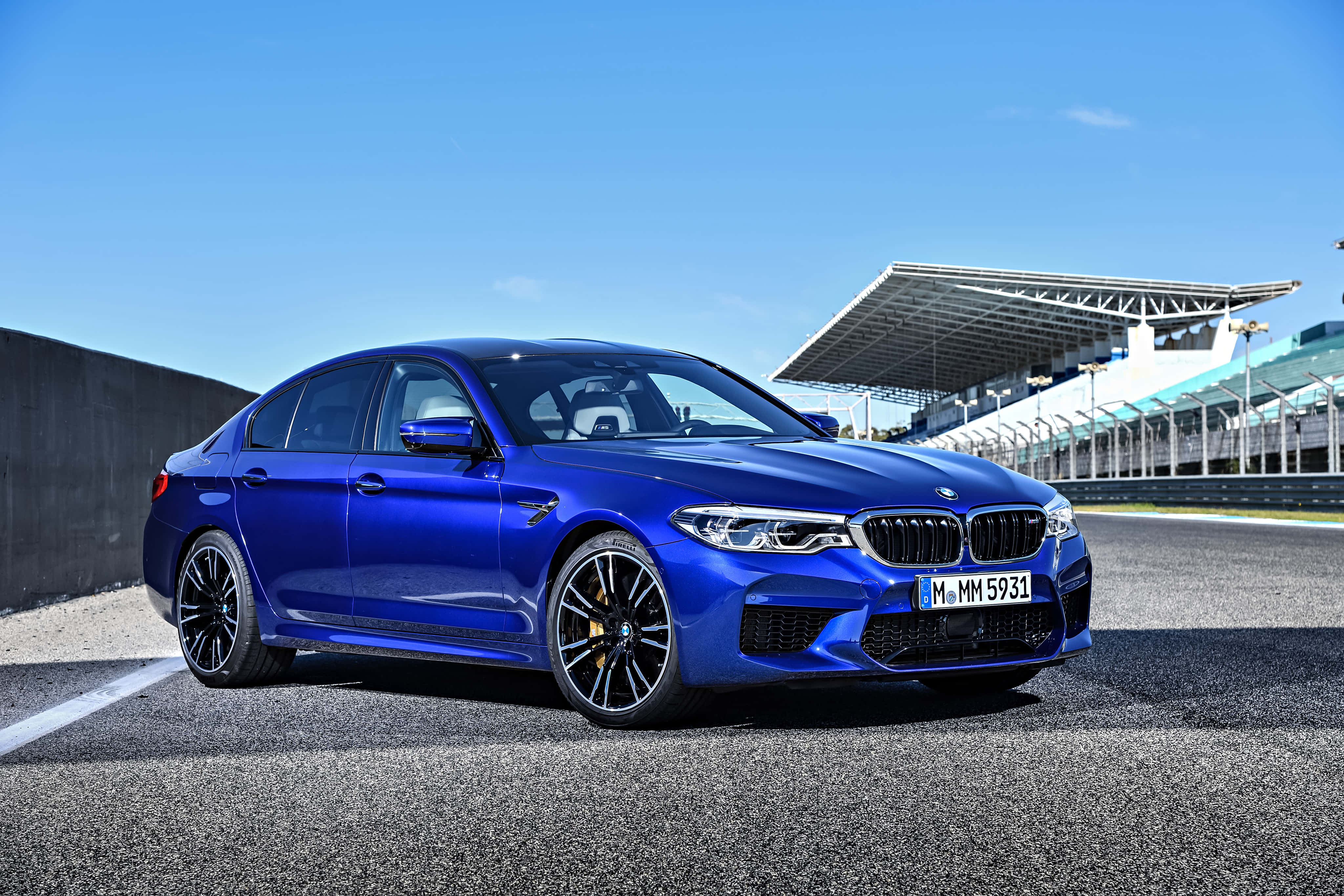 桌布 壁紙 — 一輛充滿活力的藍色BMW M5轎車在明亮的陽光下，在背景有看台的瀝青賽道上閃閃發光。