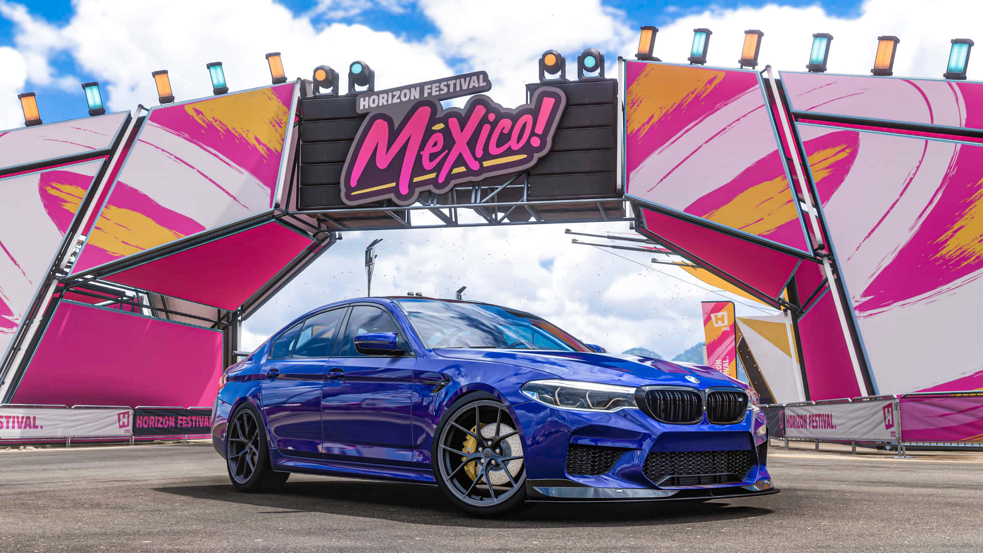 Blue M5 In Forza Horizon Mexico 壁紙 — 一輛充滿活力的藍色BMW M5轎車停放在色彩繽紛的「Horizon Festival Mexico」拱門下，拱門上有粉紅色、黃色和白色的圖案。