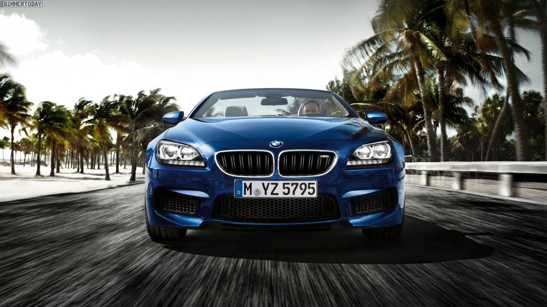 藍色 桌布 壁紙 — 一輛充滿活力的藍色BMW M6敞篷跑車在明亮的日光下沿著棕櫚樹成蔭的海岸道路飛馳。