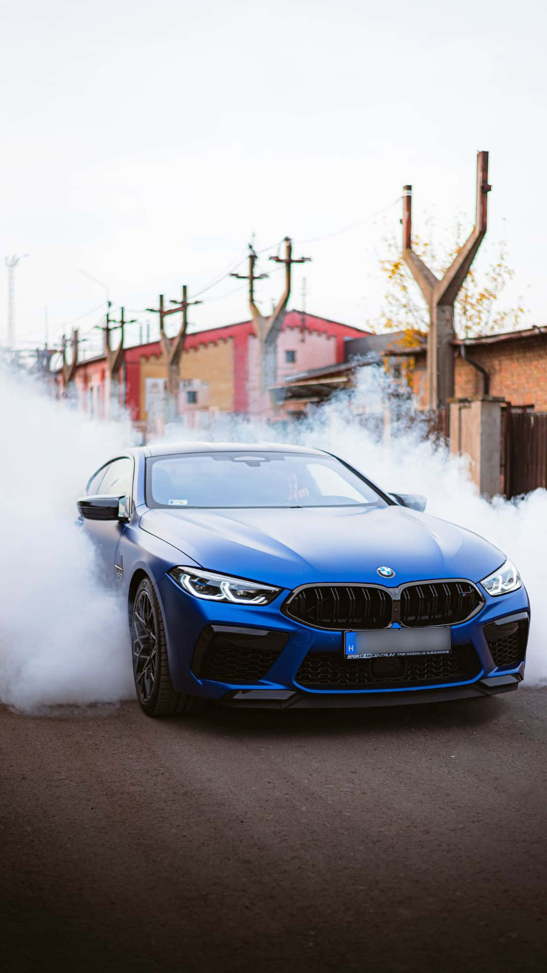 Android Bmw 桌布 壁紙 — 一輛充滿活力的藍色BMW M8在濃煙中飄移，背景是工業建築的都市街道。