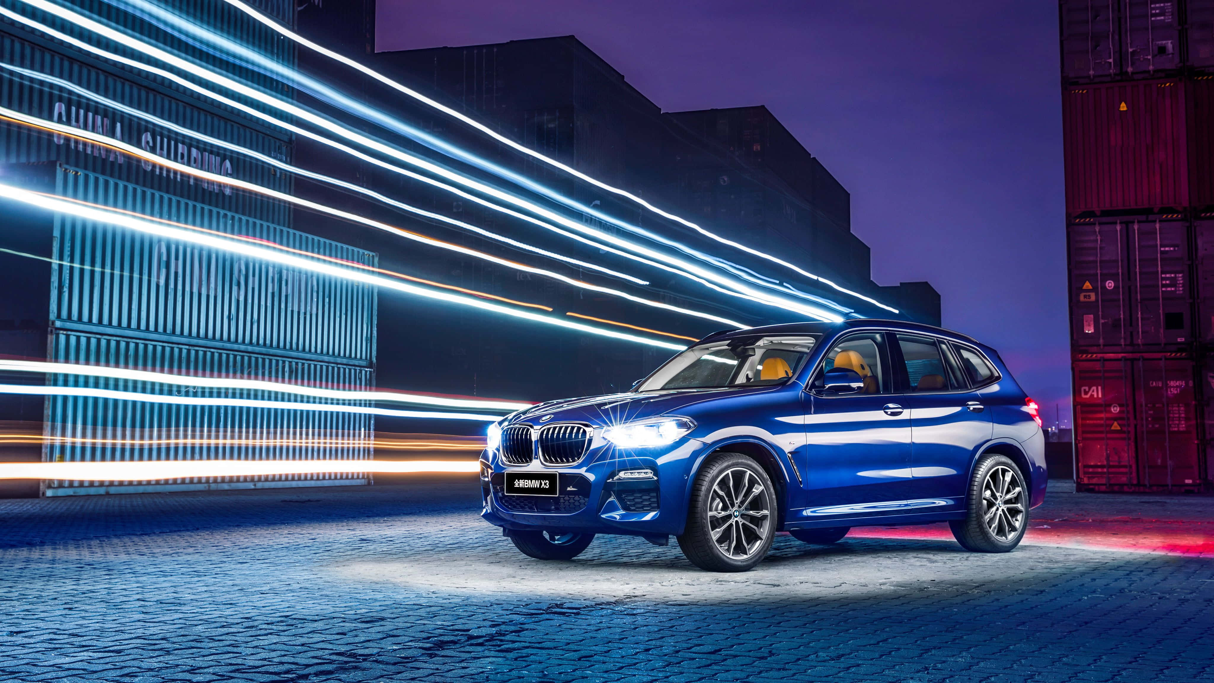 Bmw X3 桌布 壁紙 — 一輛充滿活力的藍色BMW X3 SUV在霓虹燈條下閃耀，背景是暮色城市中的貨運貨櫃。