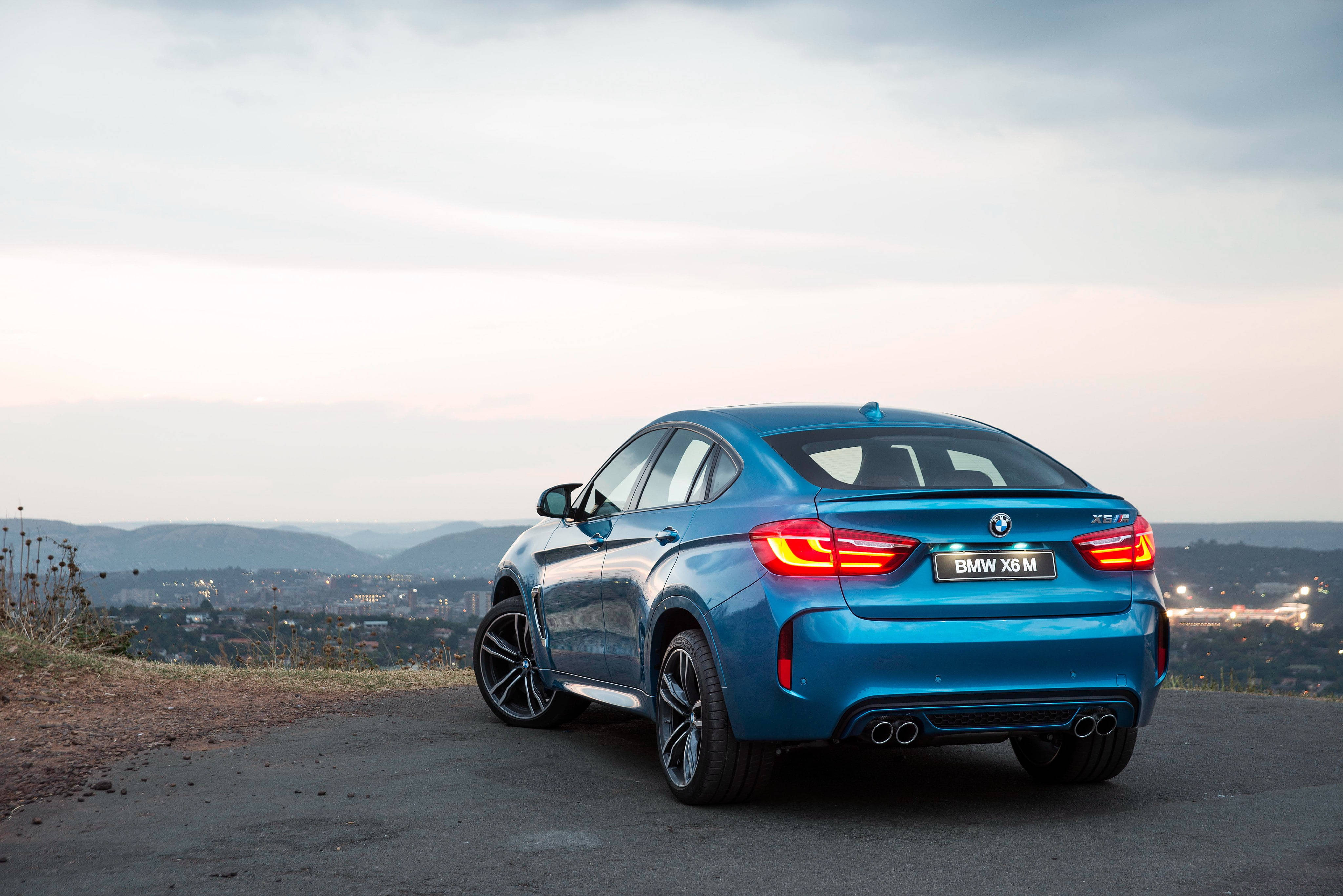 m 桌布 壁紙 — 一輛充滿活力的藍色BMW X6M運動轎跑車停在山頂上，俯瞰著黃昏時分廣闊的城市景觀。