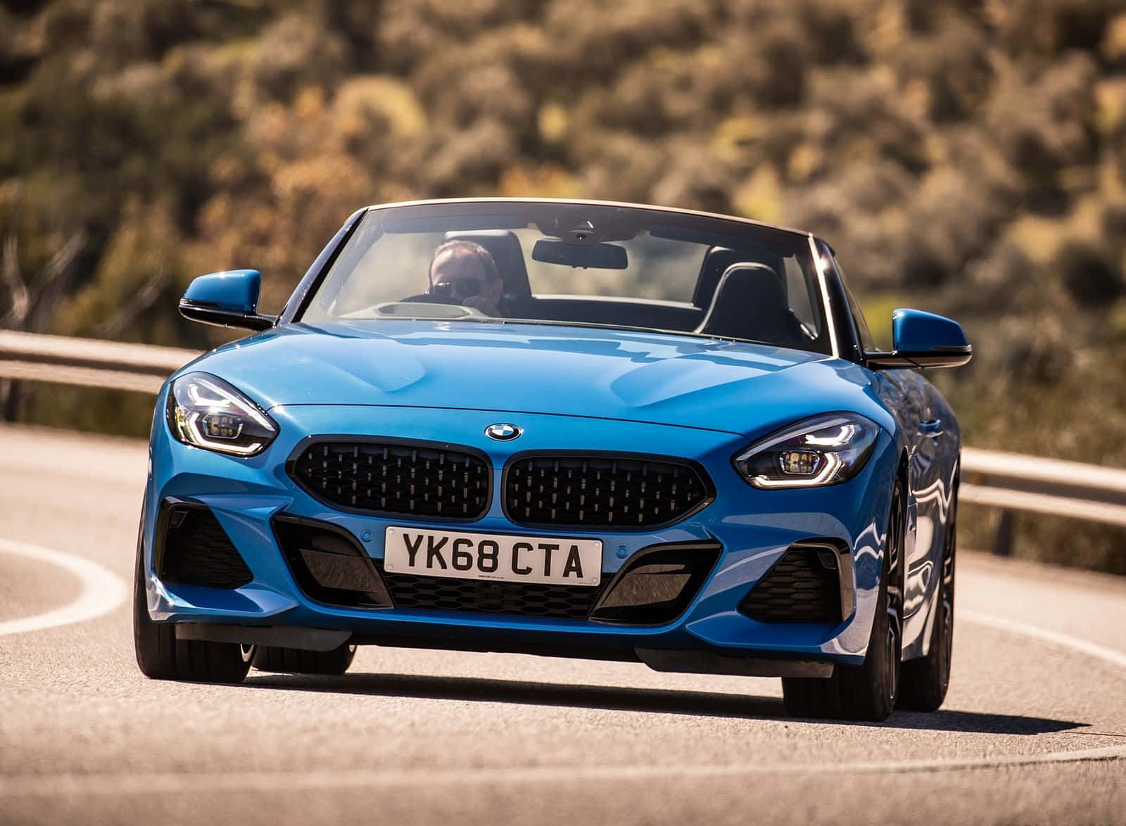 Bmw Z4 桌布 壁紙 — 一輛充滿活力的藍色BMW Z4敞篷跑車在明亮的陽光下沿著蜿蜒的山路奔馳。