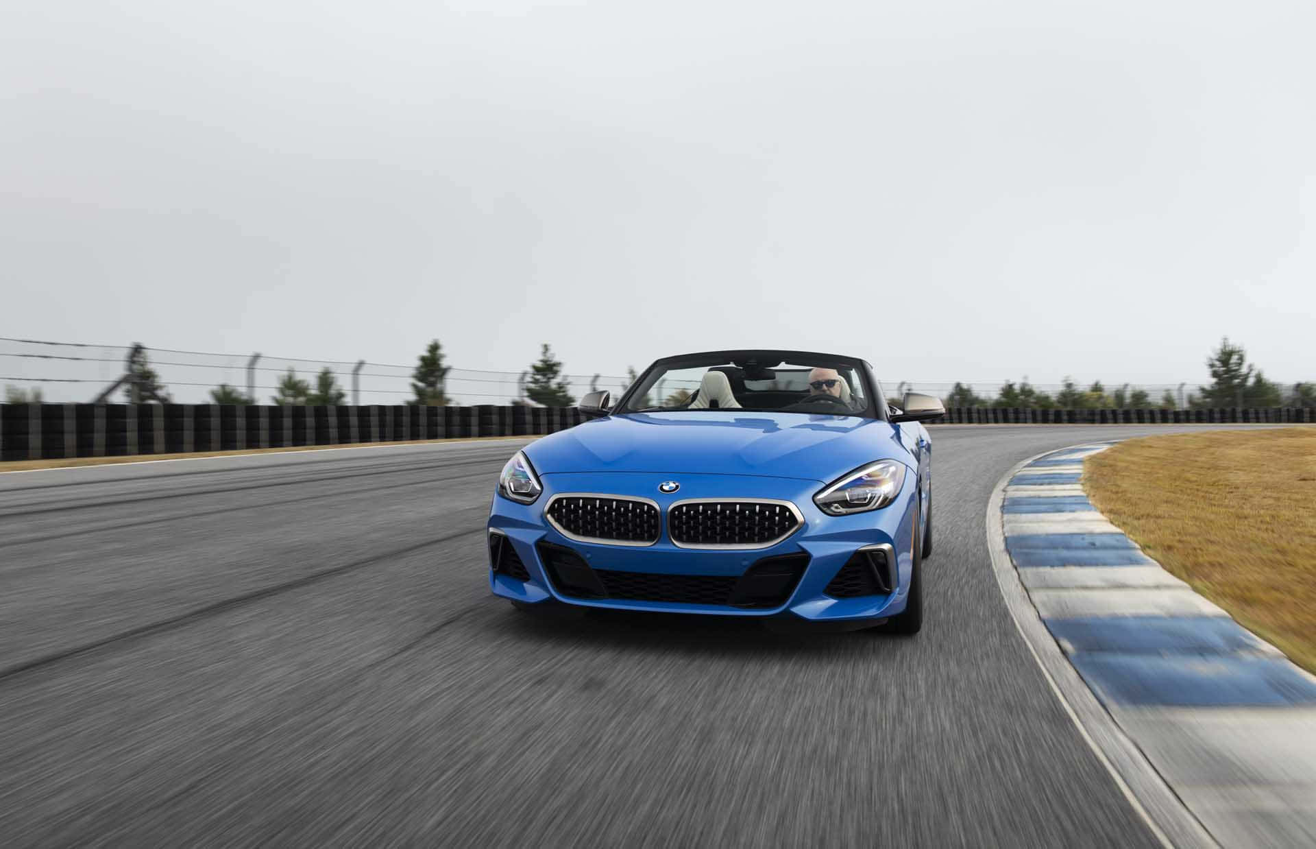 Bmw Z4 桌布 壁紙 — 一輛充滿活力的藍色BMW Z4敞篷跑車在賽道上高速行駛，帶有動態模糊效果，駕駛手握方向盤。