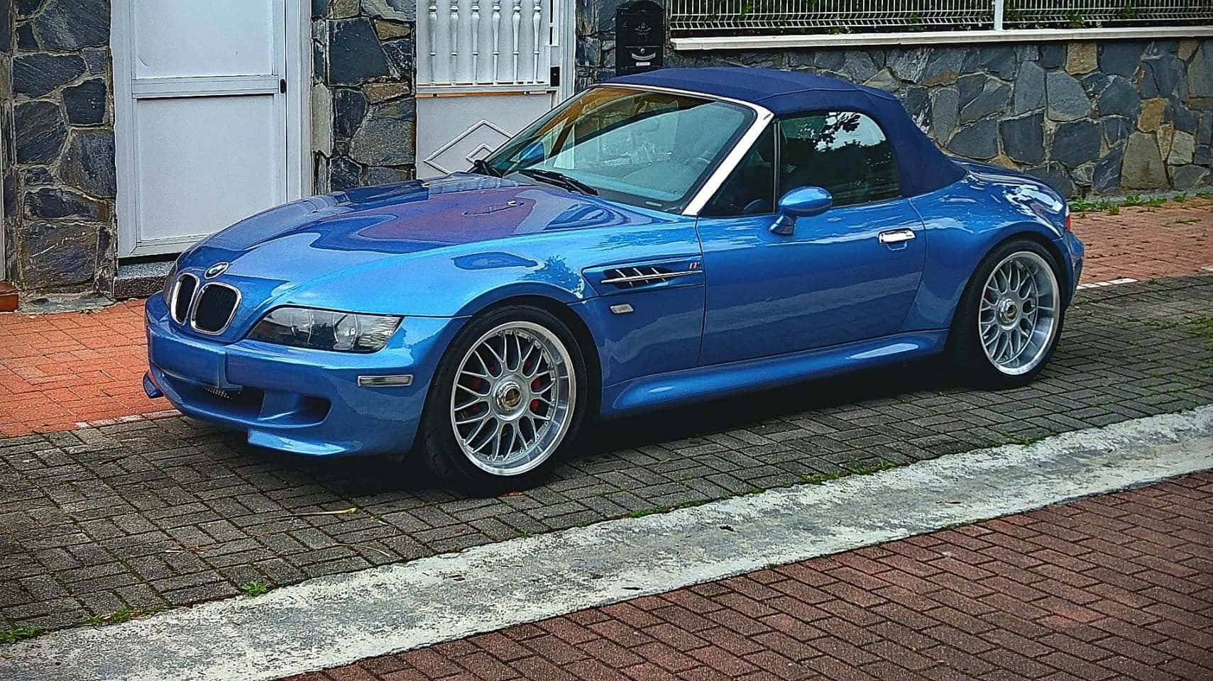 Bmw Z3 桌布 壁紙 — 一輛充滿活力的藍色BMW Z8敞篷車停在石牆旁的磚砌車道上。