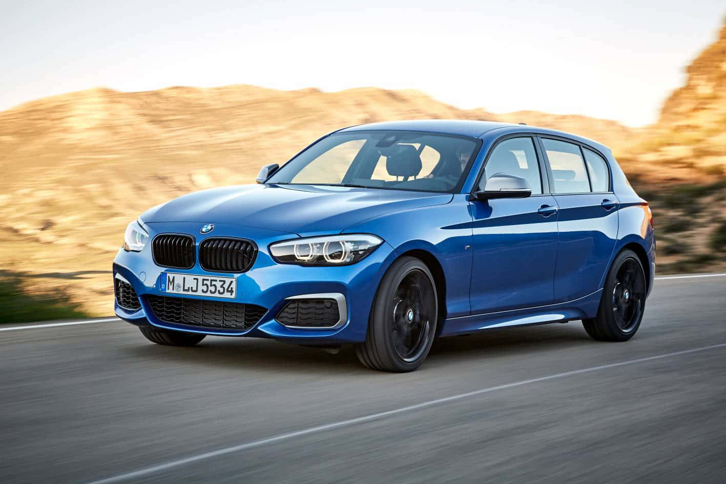 Bmw 1 Series 桌布 壁紙 — 一輛充滿活力的藍色BMW掀背車在沙漠公路上飛馳，背景是模糊的金色山丘。