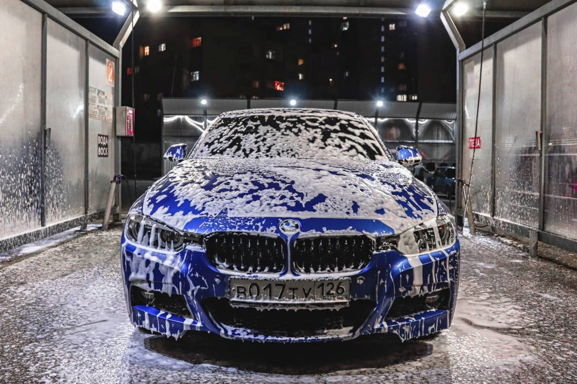 Wash 桌布 壁紙 — 一輛充滿活力的藍色BMW跑車被厚厚的白色泡沫覆蓋，在夜間的室內洗車場中於明亮的燈光下清洗。