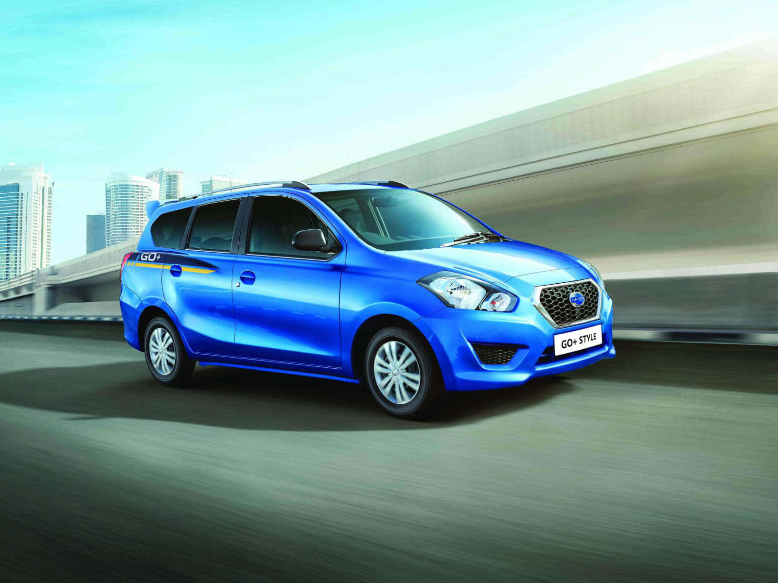 Datsun 桌布 壁紙 — 一輛充滿活力的藍色Datsun GO+ Style小型貨車在現代高速公路上疾馳，背景是模糊的城市摩天大樓。