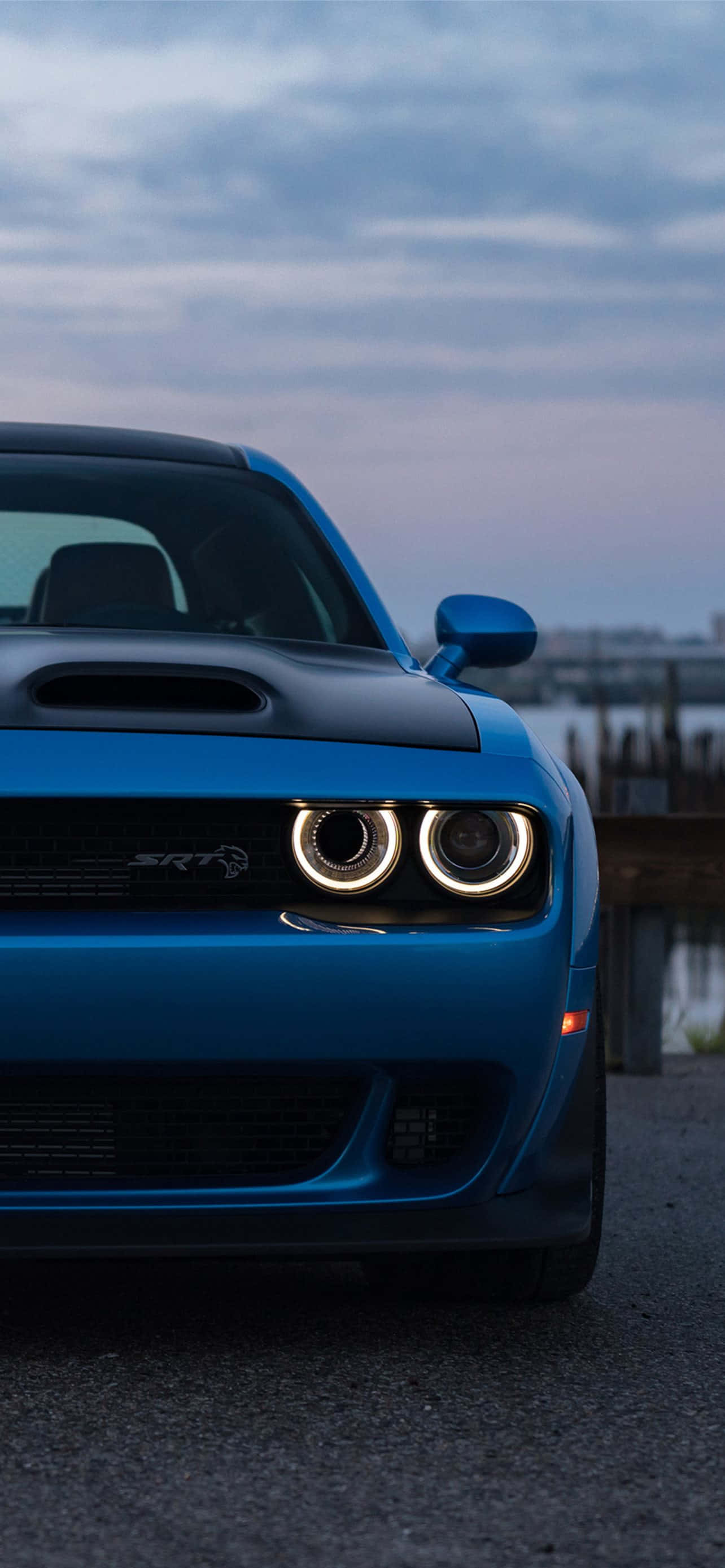 汽車 4K 桌布 壁紙 — 一輛充滿活力的藍色Dodge Challenger SRT Hellcat，帶有發光的圓形頭燈，停在黃昏的瀝青路上。
